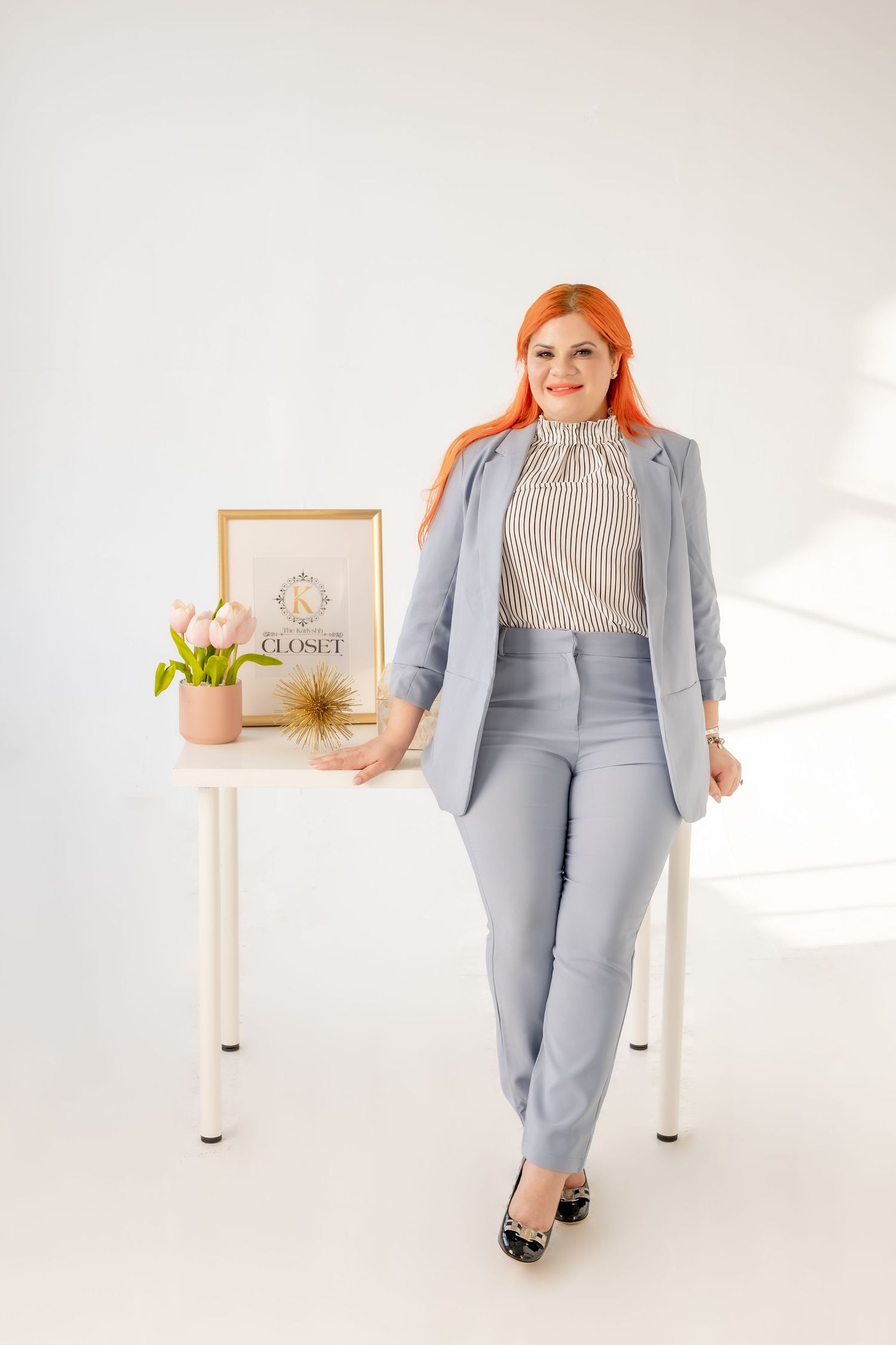 Professional woman in gray business suit standing next to office desk with decorative accessories.