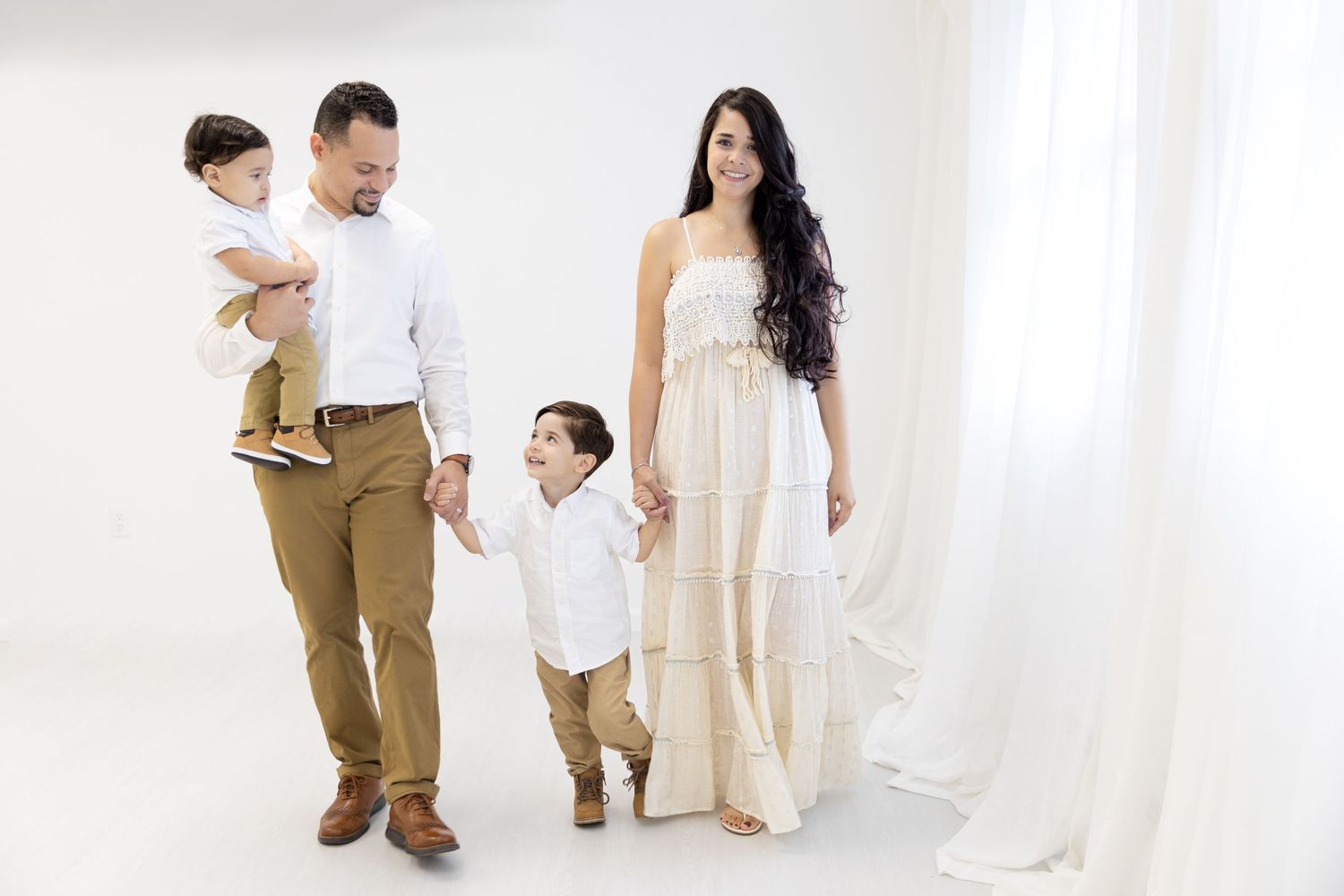 Family photoshoot in an all-white studio with coordinated neutral outfits.