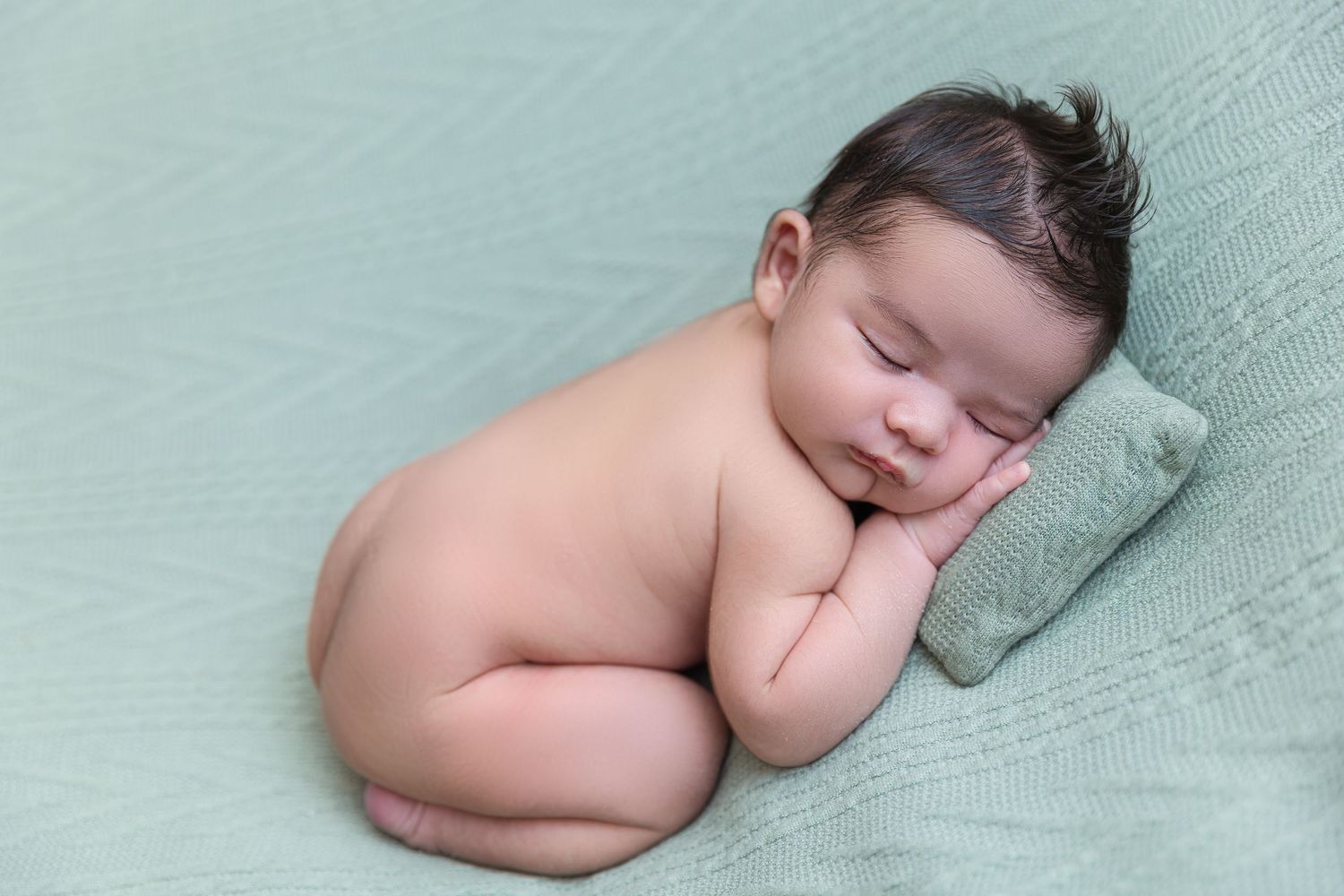 Peaceful sleeping newborn baby curled up on mint green blanket.