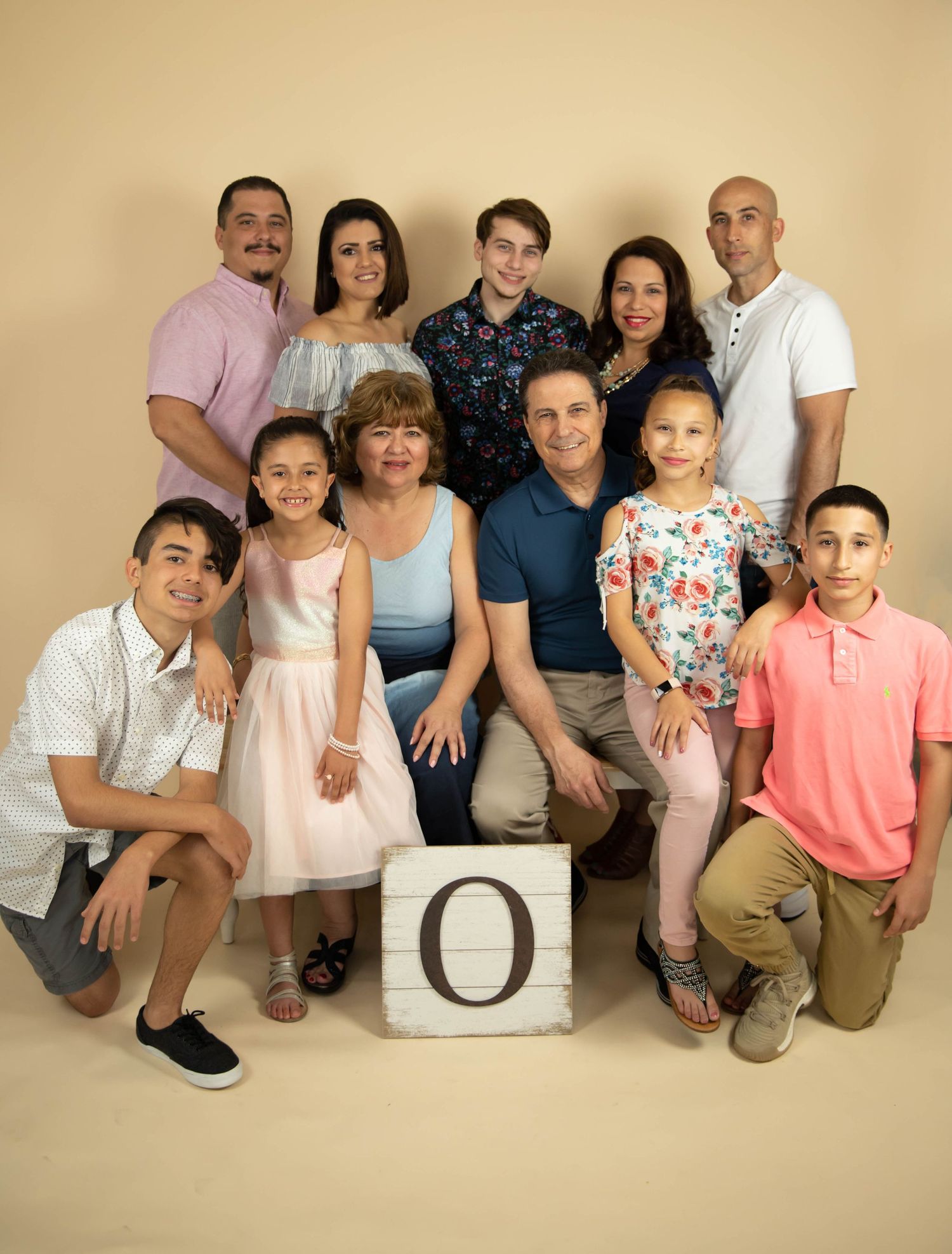 Multi-generational family portrait with members arranged around a decorative block against beige backdrop.