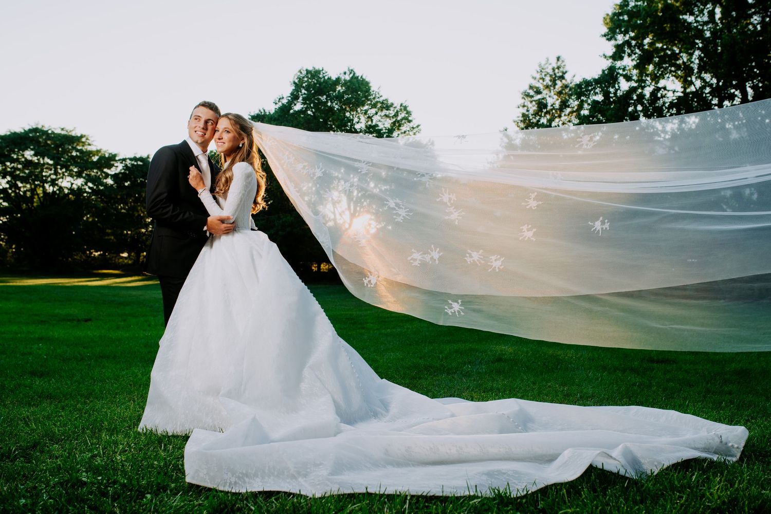 A flowing white wedding veil catches the breeze in an outdoor garden setting during a romantic photo session.