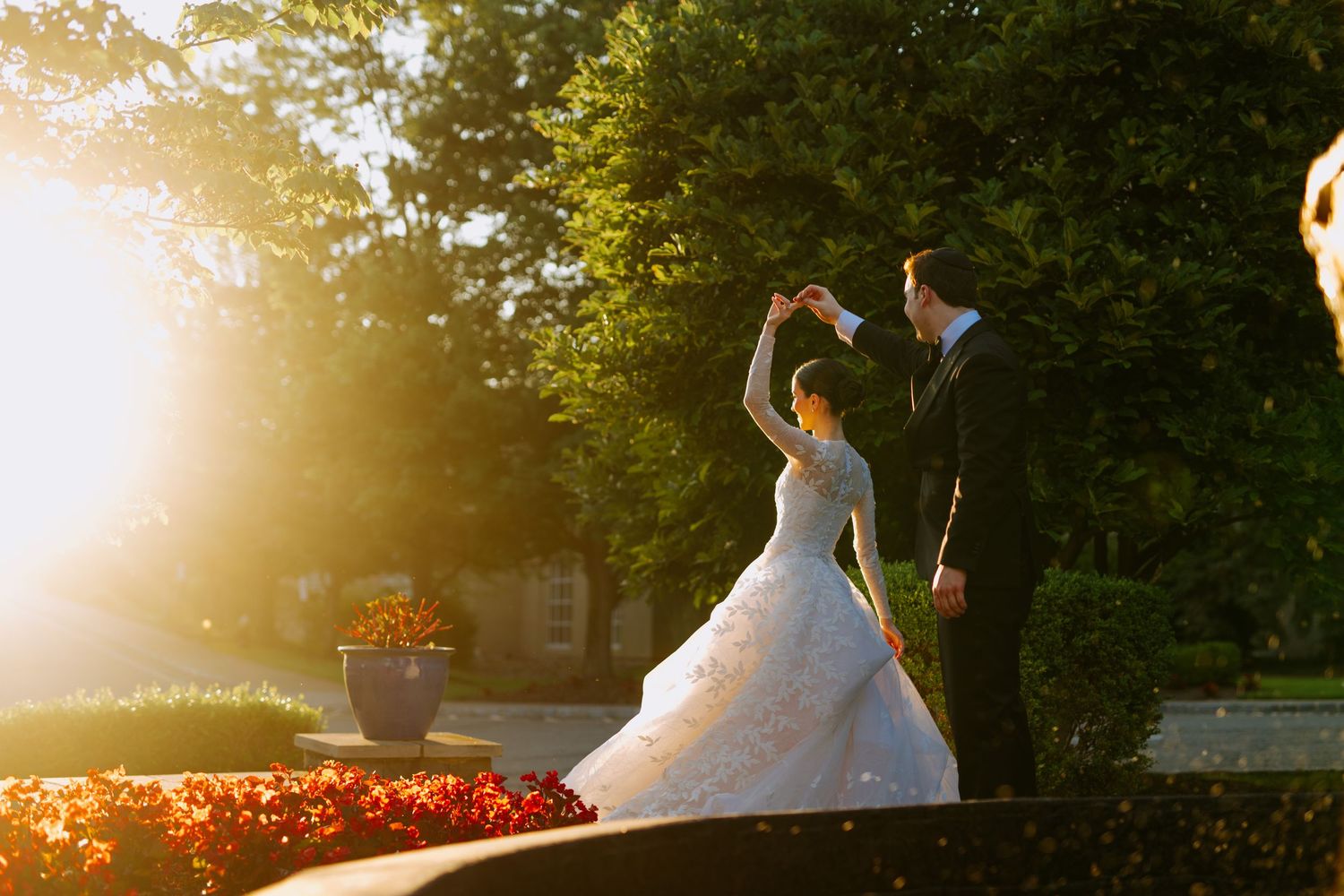 Couple dancing together in a garden at sunset with bright golden sunlight streaming through the trees.