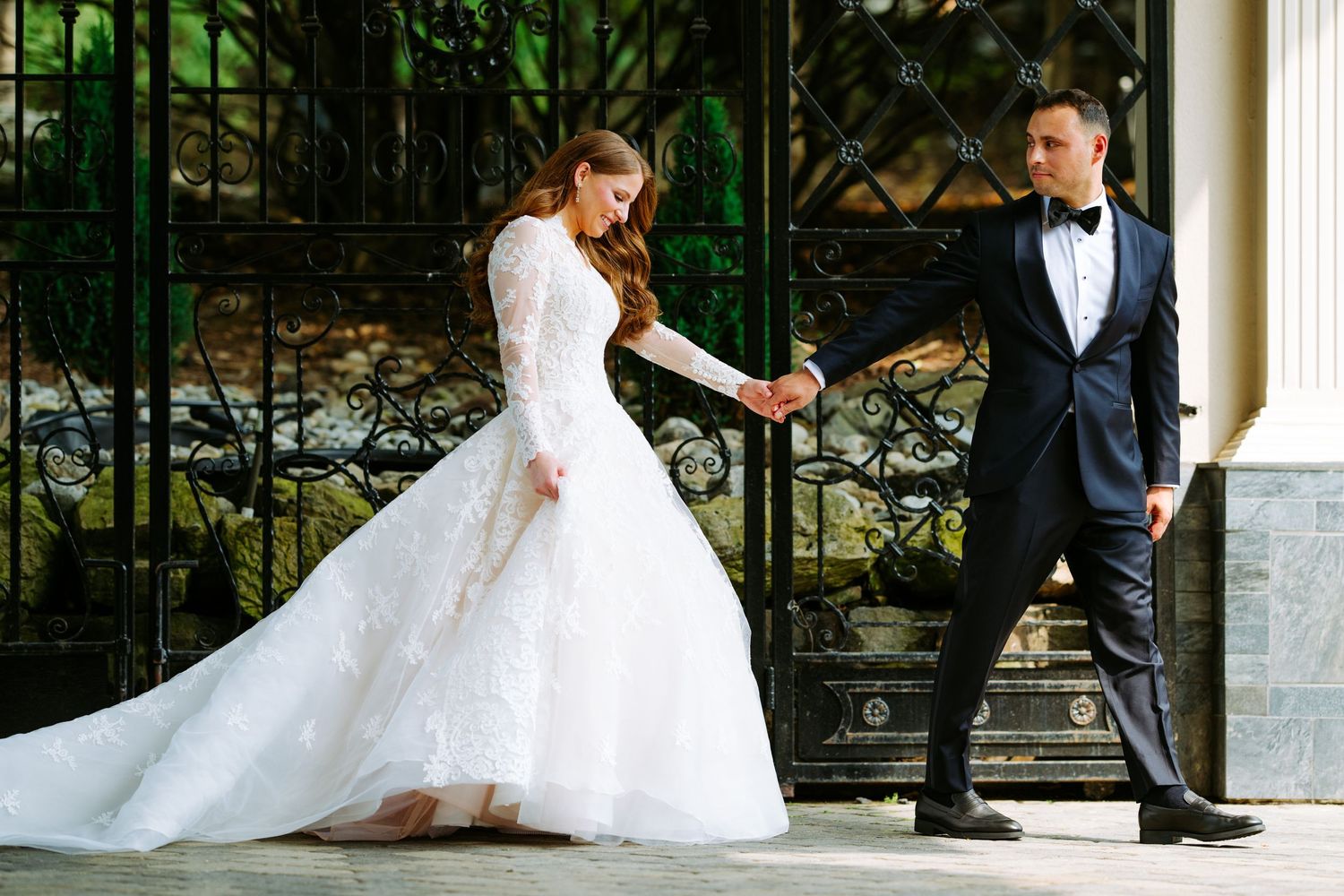 Elegant wedding couple shares romantic moments in a garden setting with white columns and lush greenery.