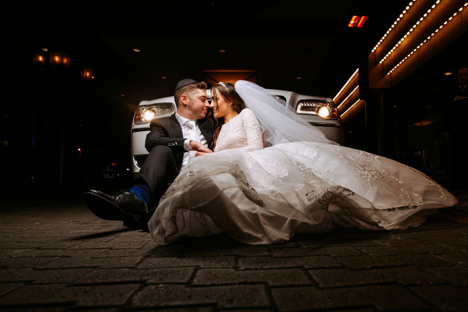 Romantic wedding couple embraces on a dark dance floor illuminated by dramatic lighting during their first dance.