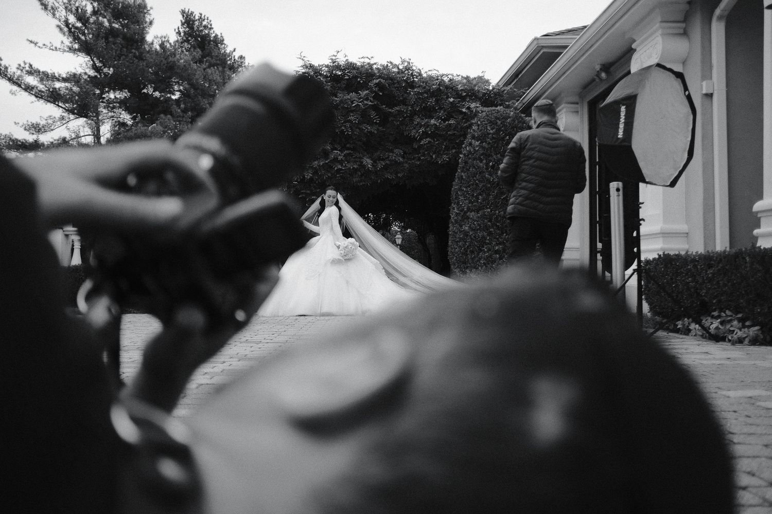 A black and white close-up photograph showing hands adjusting camera settings outdoors.