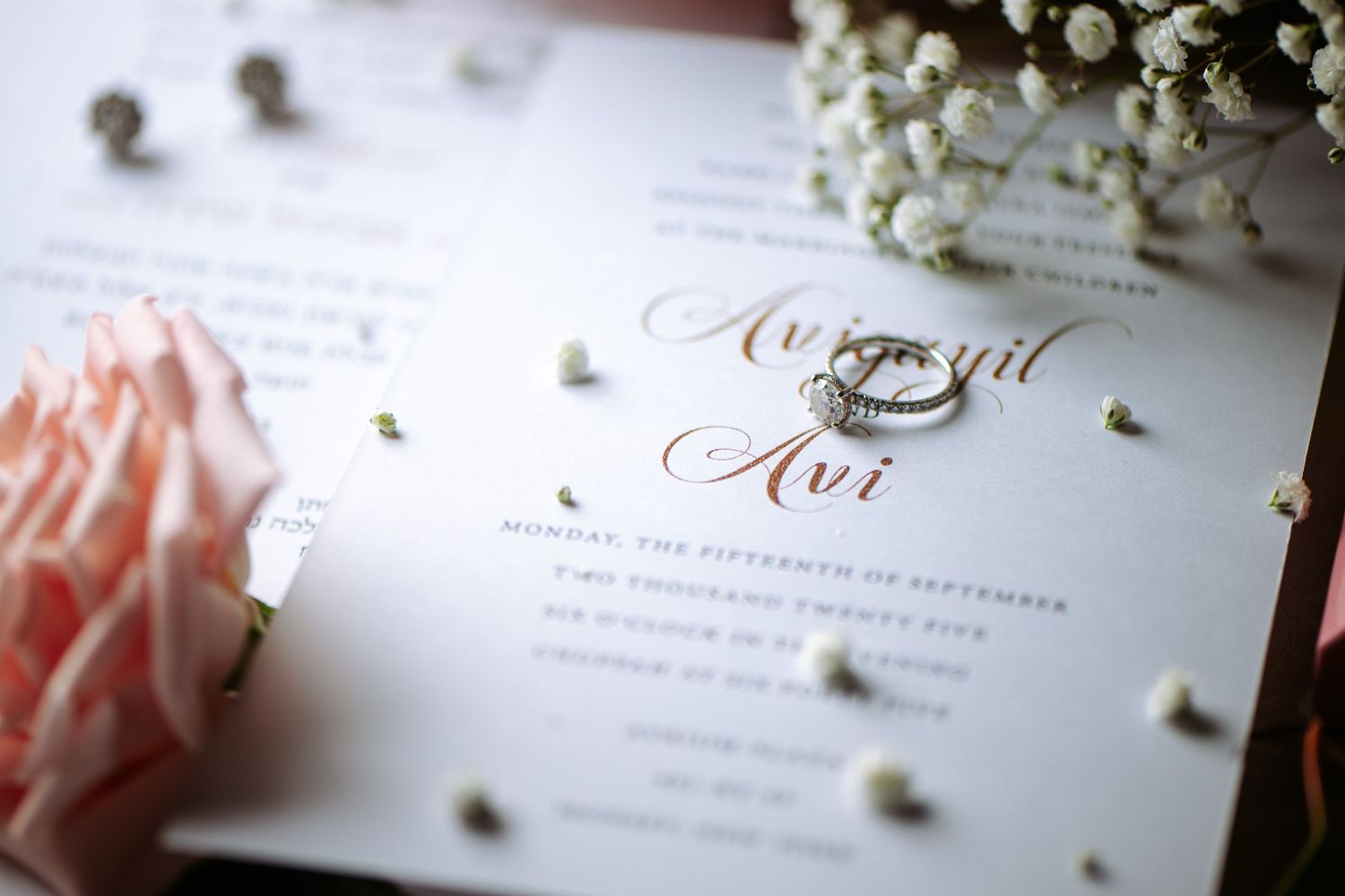 Wedding invitation cards with elegant calligraphy and delicate pink flowers lay arranged on a white surface.