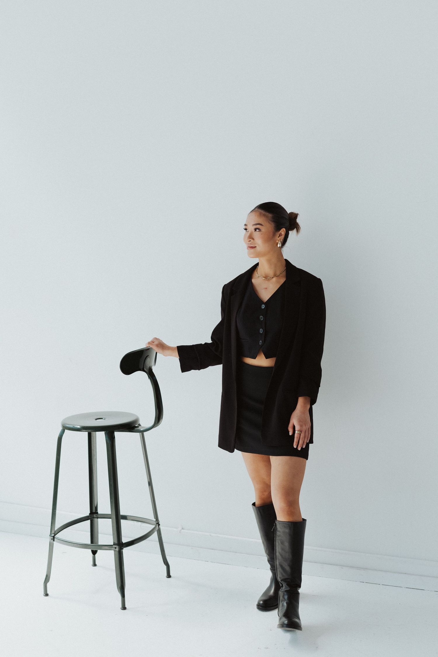 Fashion photoshoot with black outfit and industrial stool against minimalist backdrop.