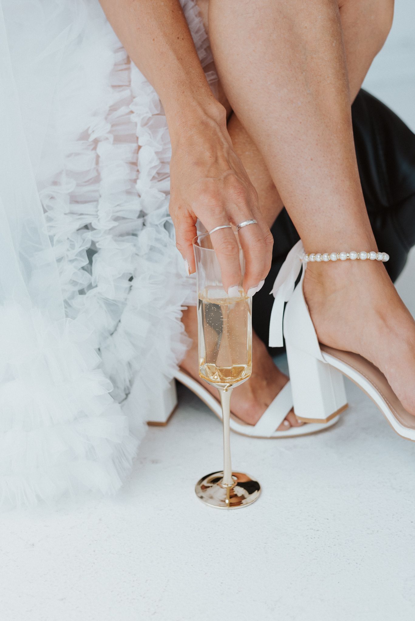 Close-up of elegant white heels and pearl anklet against white background.