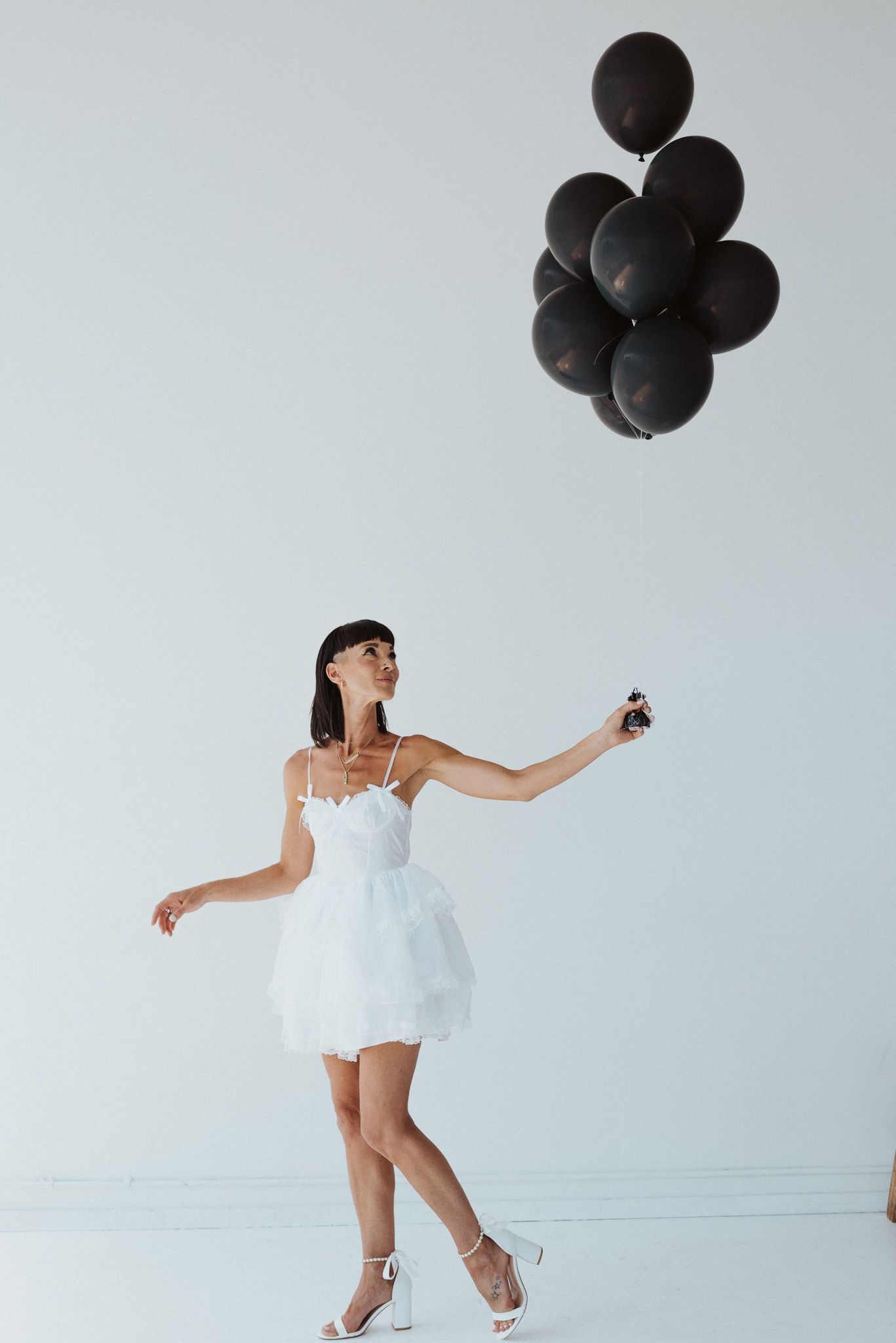 Artistic dance pose with black balloons against white studio background.