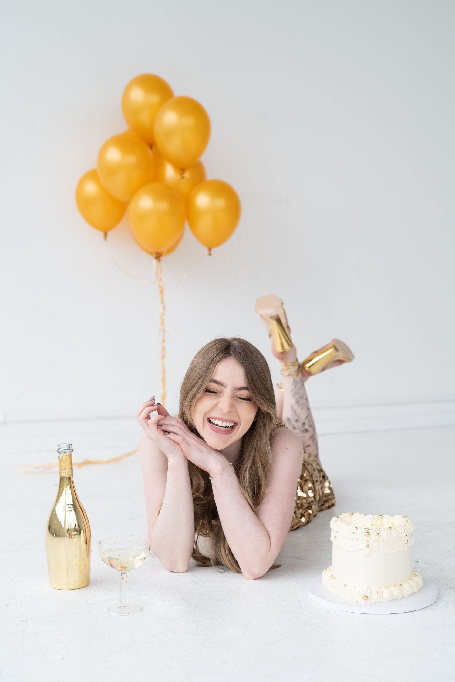 Celebratory scene with gold balloons, champagne, and white cake against a bright minimal background.
