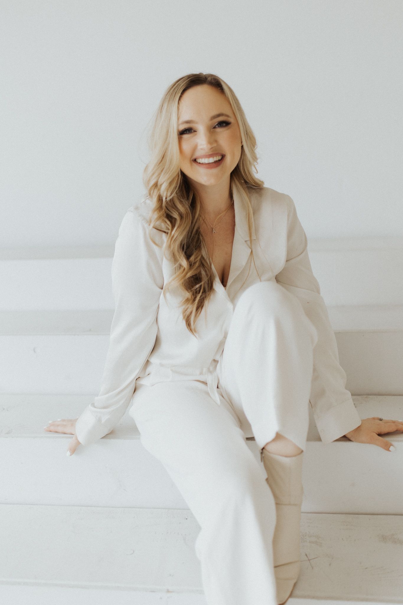 Professional studio photoshoot with white blazer outfit against light background.