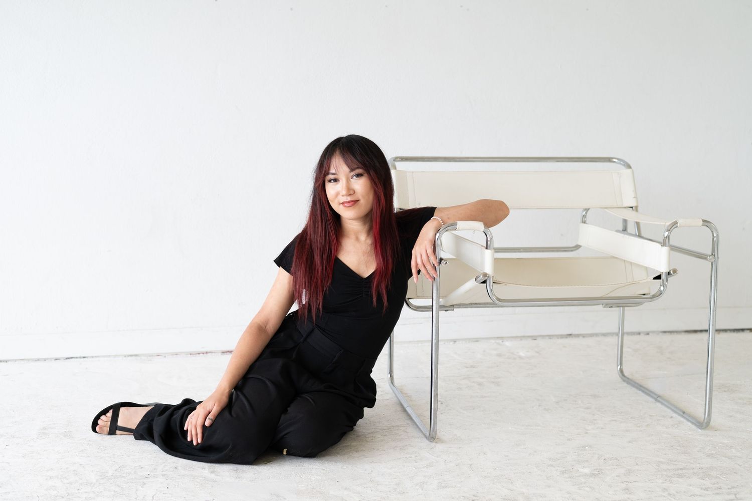 Woman in black outfit posing on floor with white furniture.
