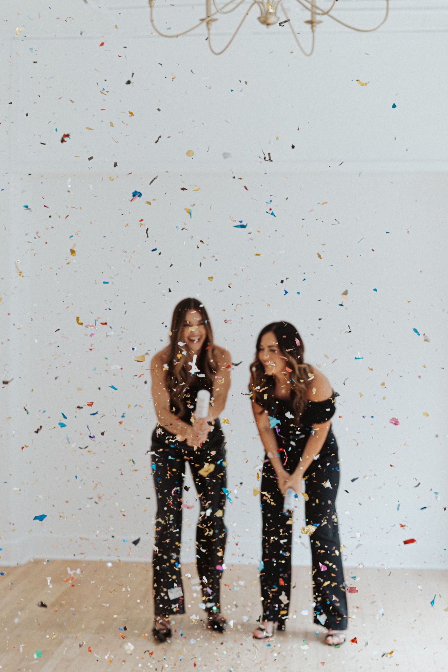 Two friends in black outfits playing with falling confetti against white backdrop.
