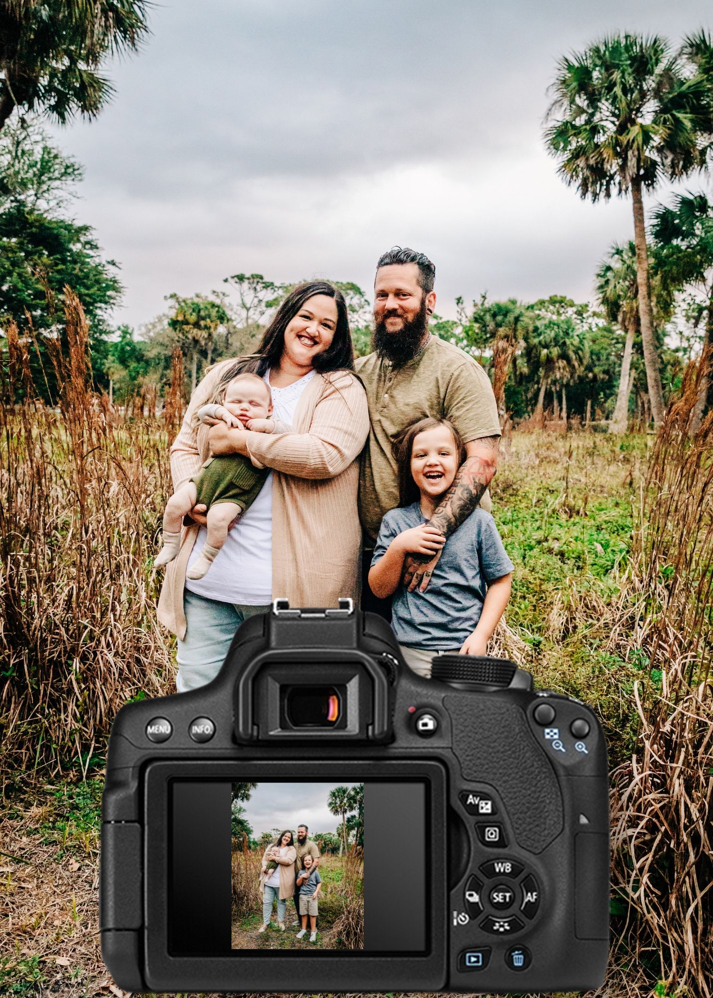 Camera display shows family photo shoot in progress outdoors with tall grasses and palm trees in background.