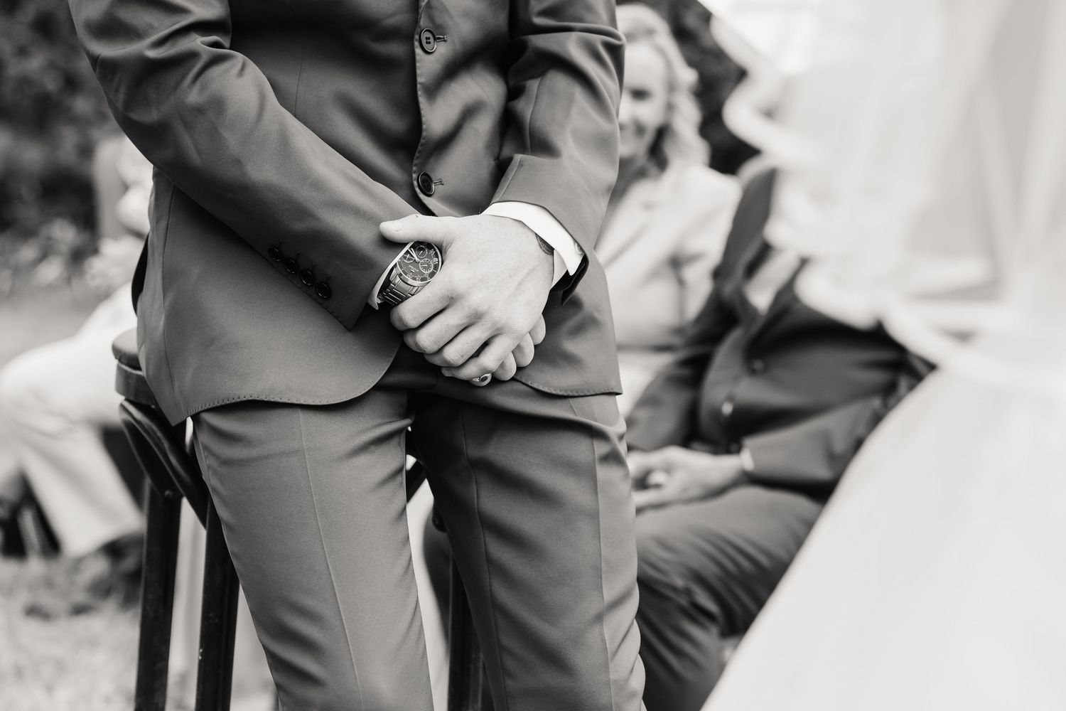 Black and white photo of a groom in a suit with a watch, clasping hands during an outdoor wedding ceremony at Moor Farm, Weymouth Dorset