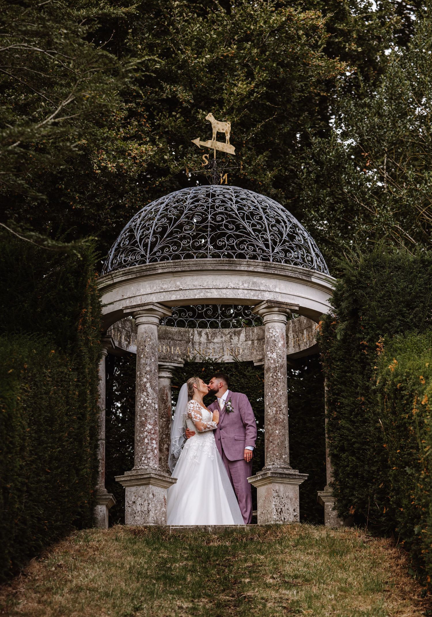 Elegant wedding couple photographed in a series of romantic poses under an ornate stone gazebo in a garden setting.