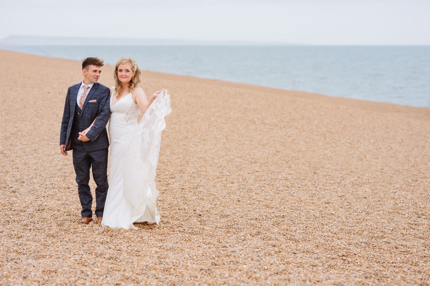 Bride and groom on Chesil Beach following their wedding at Abbotsbury Subtropical Gardens. Candid wedding photographer based in Weymouth