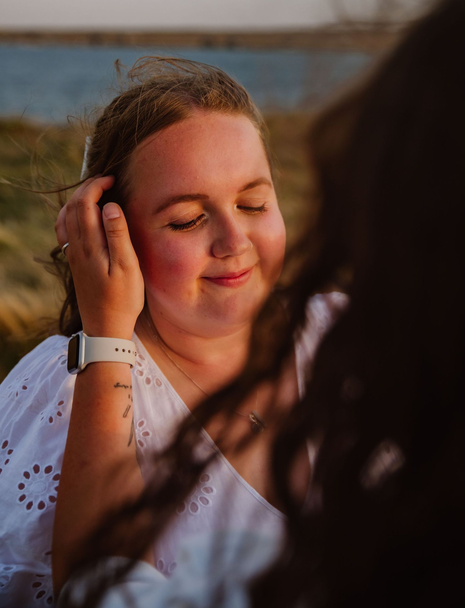 A person in a white eyelet dress smiles peacefully with closed eyes while resting their hands on their face. Relaxed Dorset photographer