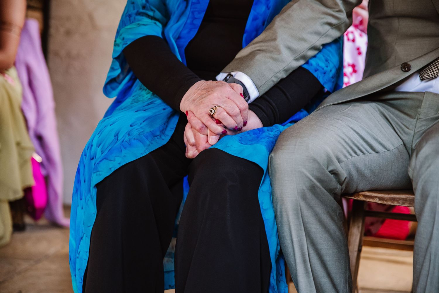 Elderly couple holding hands tenderly while seated, wearing formal attire with a blue shawl, symbolizing love and togetherness.
