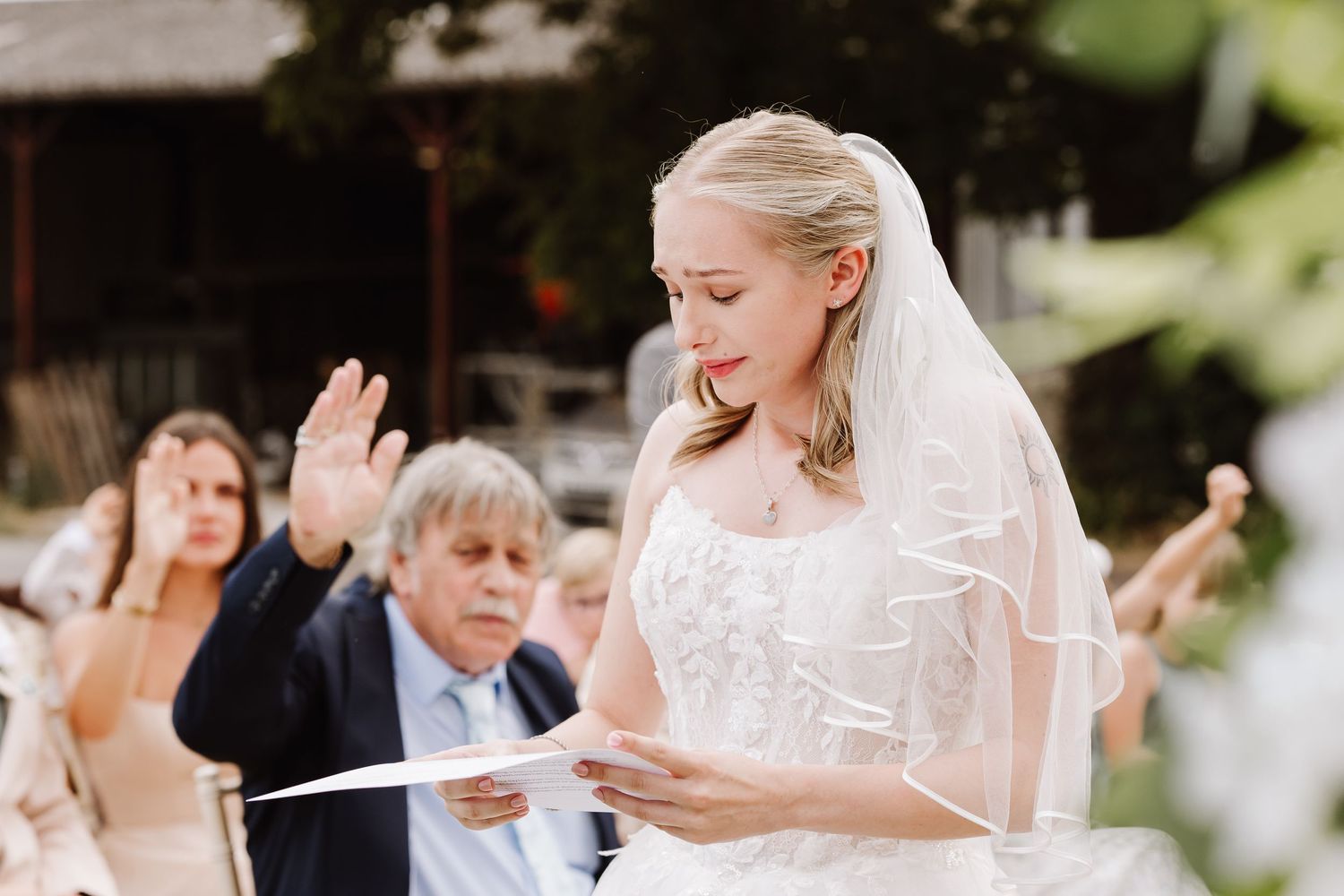 Bride in white lace gown and veil reads wedding vows at Moor Farm, Weymouth Dorset during outdoor ceremony.