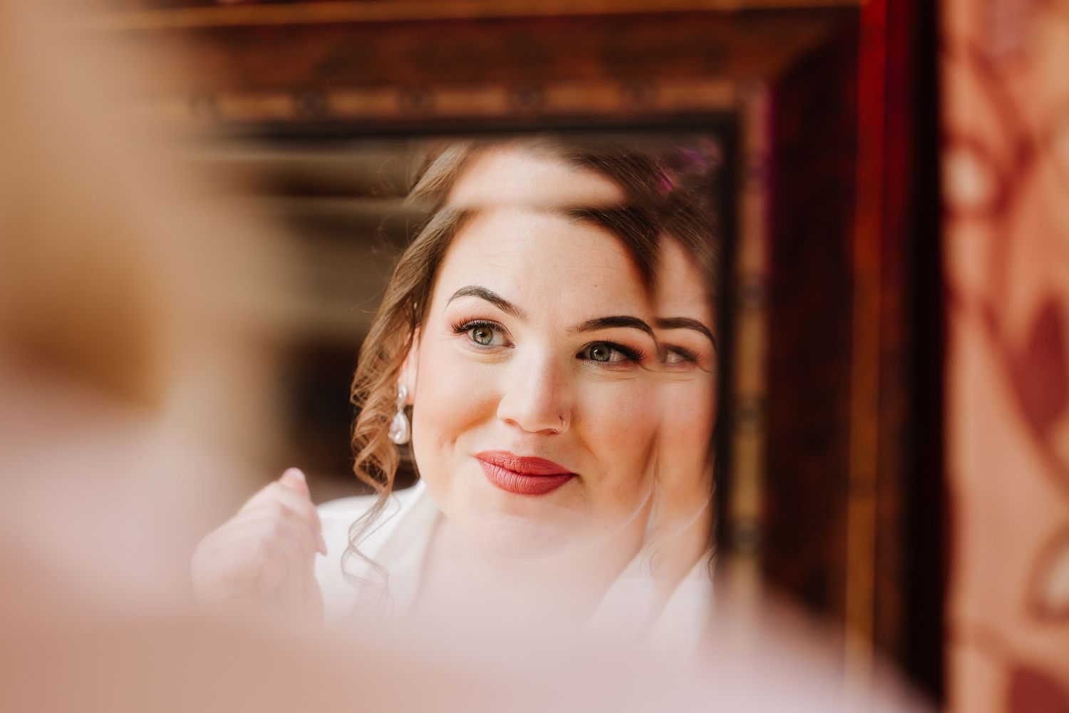 Bride admiring her wedding makeup in an ornate mirror, showcasing elegant updo and red lips at Southampton wedding