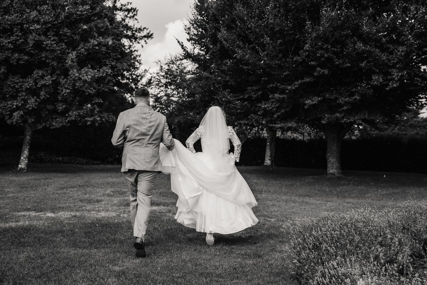 black and white photograph showing a couple walking through a park holding hands at Kingston Maurward Estate a wedding venue Dorchester