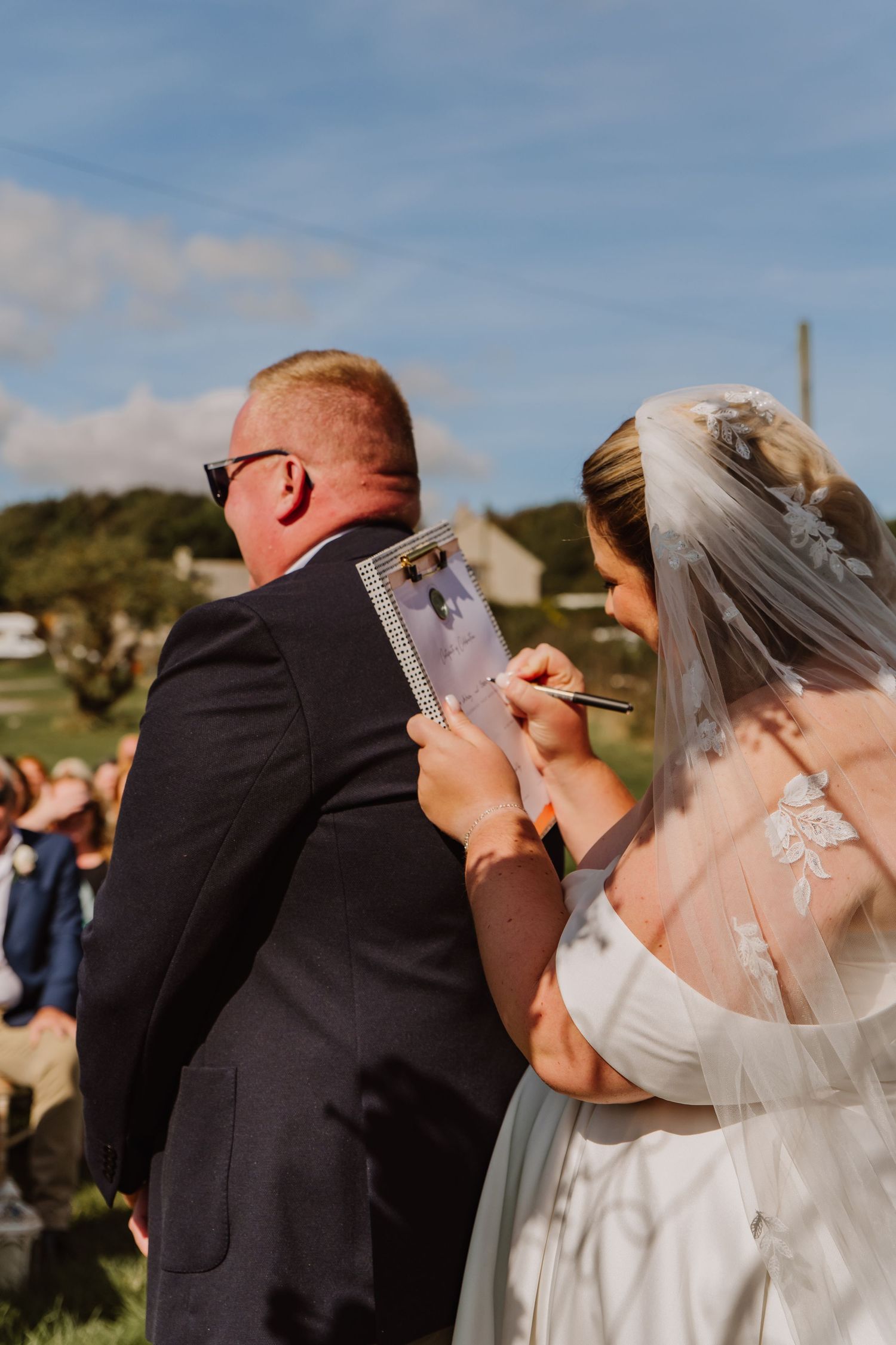 Bride signs marriage certificate on grooms back at Moor Farm Barn Outdoor wedding, Chickerell, Dorset. Dorset wedding photographer.