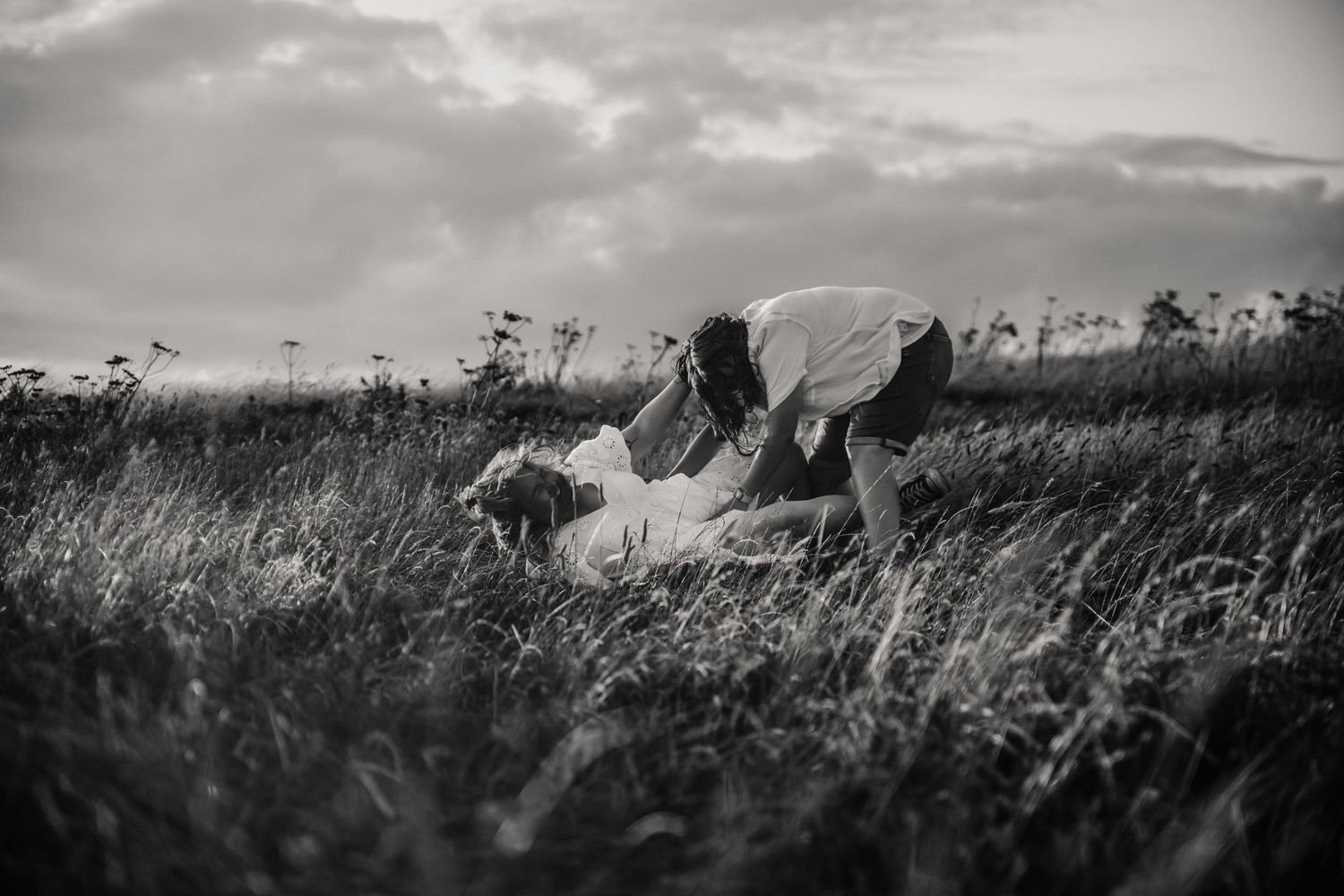 Two brides fall on the ground in a meadow during an engagement shoot in Weymouth, Dorset. Relaxed Dorset Wedding photographer