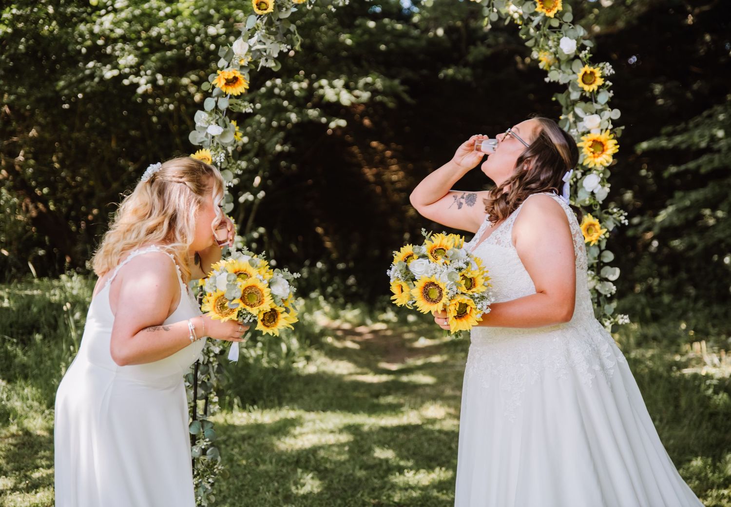 Gaggle of Geese Tipi outdoor wedding venue in Dorset. Sunflower wedding bouquet and sunflower arch. Brides take a shot. LGBTQ+ wedding photo