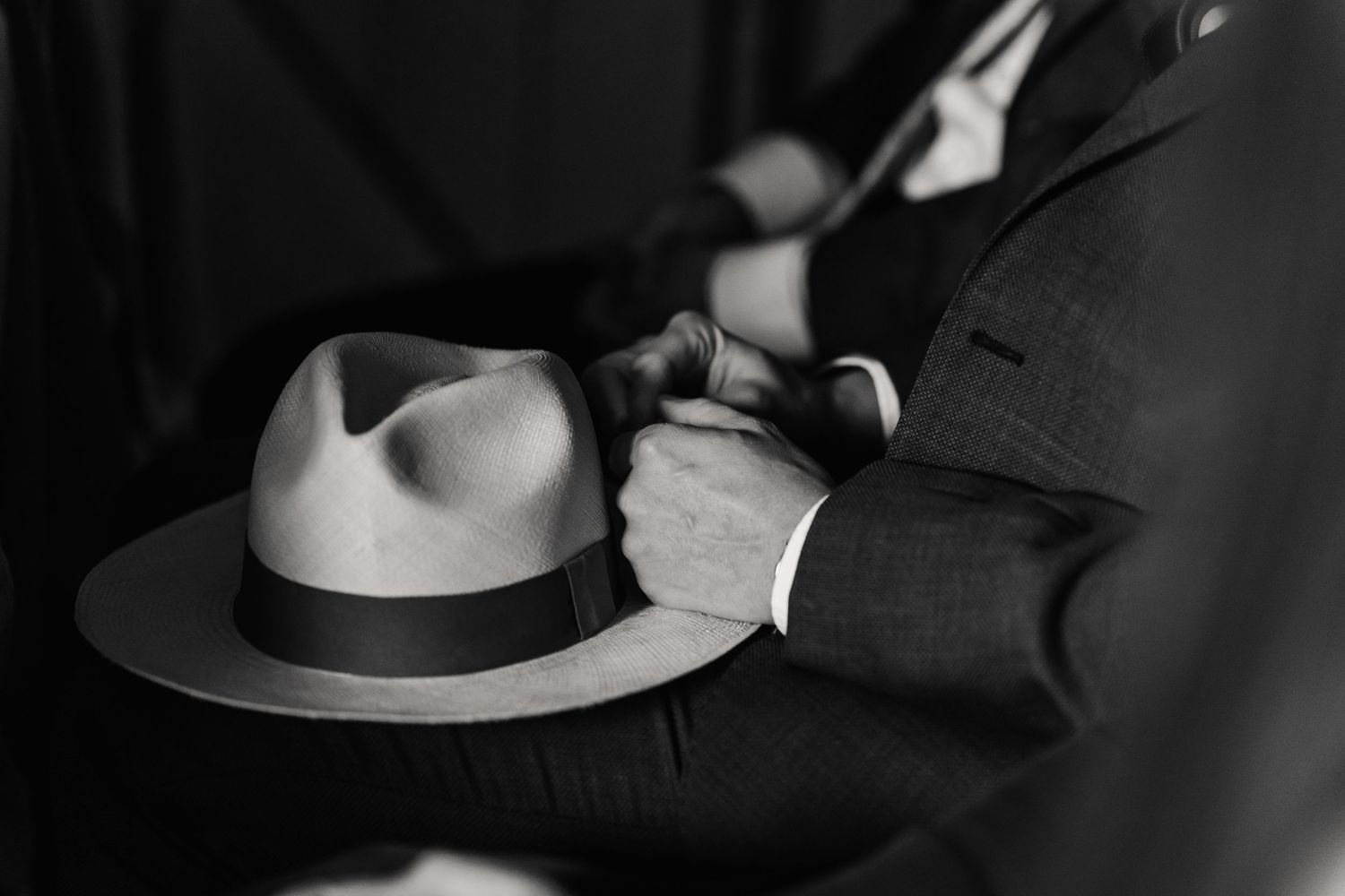 Black and white photo of a man in a suit holding a classic fedora hat with a dark band.