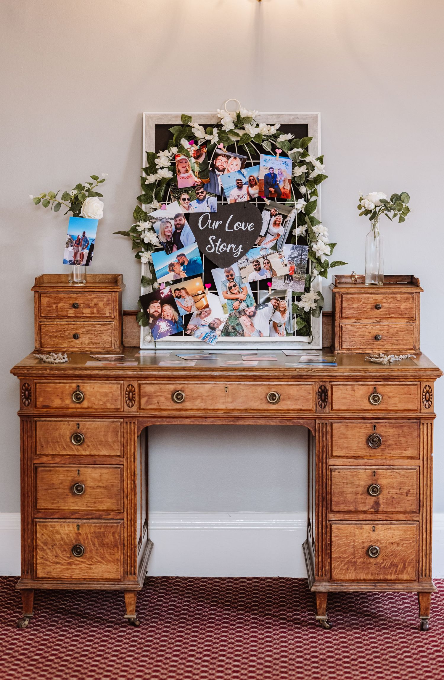 Vintage wooden vanity desk with ornate drawers and decorative photo frames displayed on top against a beige wall.
