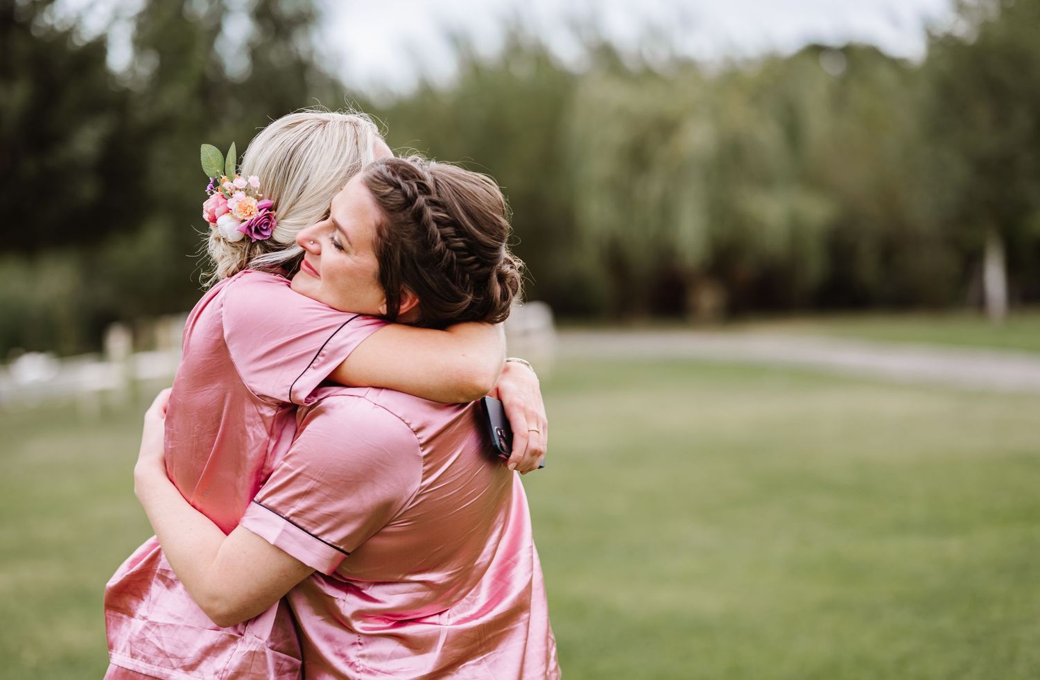 Two people in pink pjs share a warm embrace on a grassy lawn with trees in the background at the waterside country barn and mill, Taunton