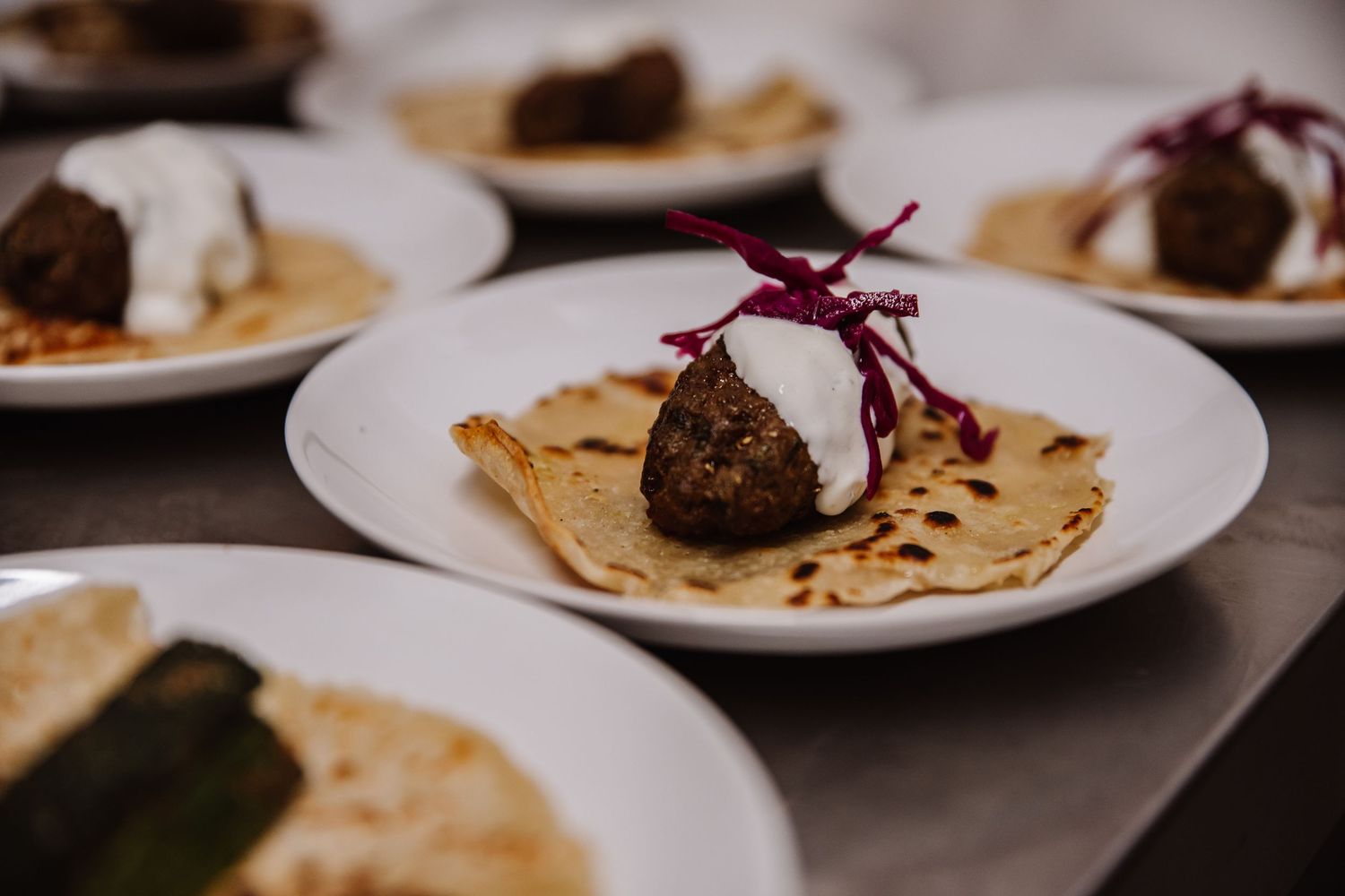 Gourmet Kofte on flatbread topped with white sauce and red garnish, served on white plates at the Cornish Place wedding venue.