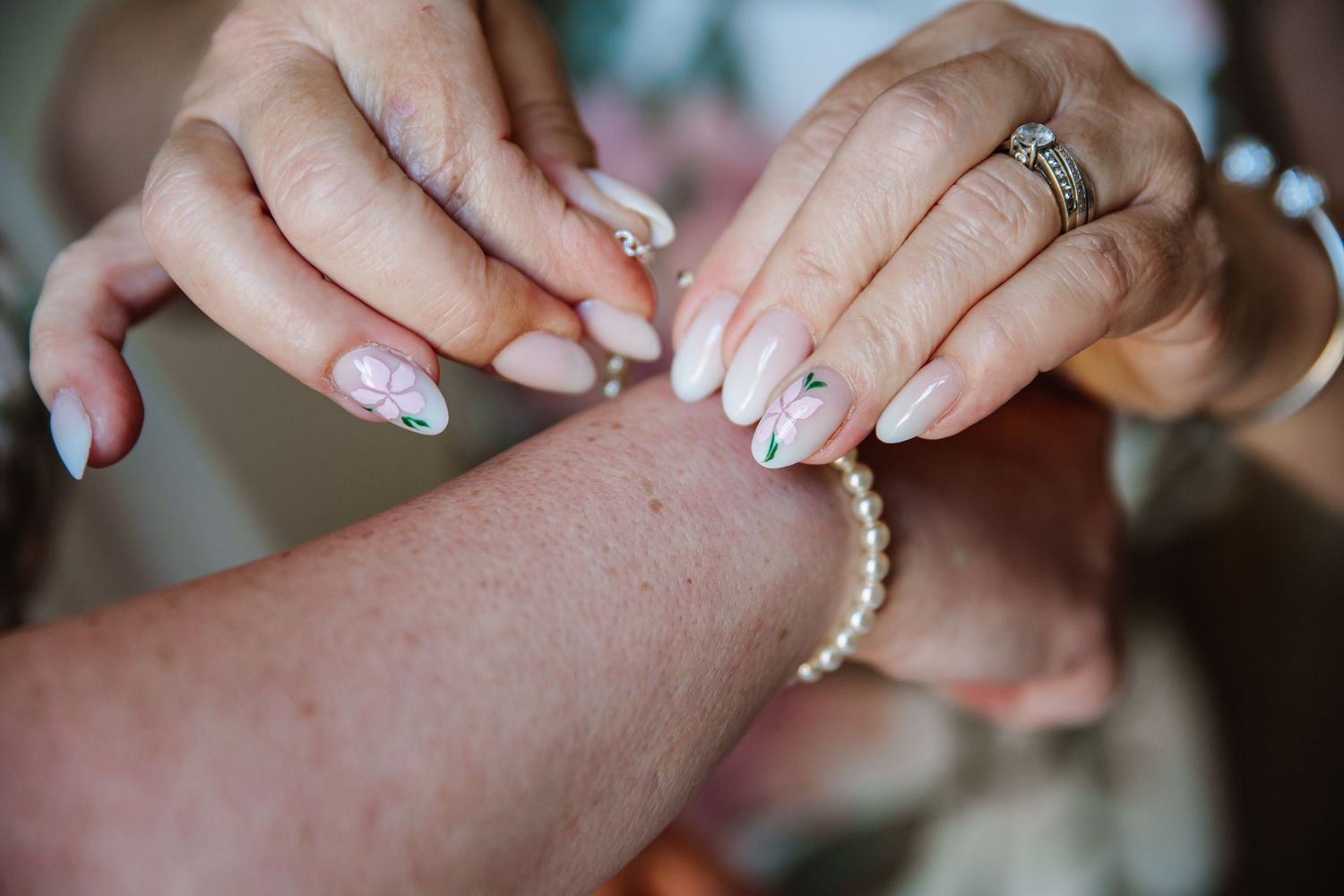 Close-up of hands fastening a pearl bracelet, featuring elegant floral nail art and a diamond engagement ring at Iwerne House, Clayesmore