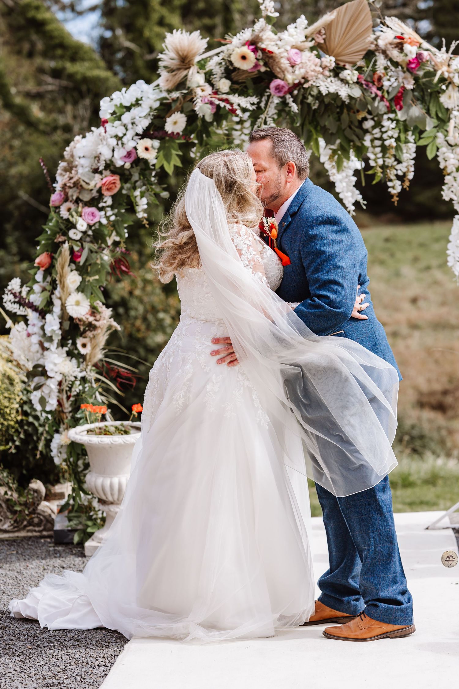 Bride and Groom at Holbrook Manor  wedding venue Somerset. Surrounded by floral arch way. Groom in blue suit. Candid wedding photographer