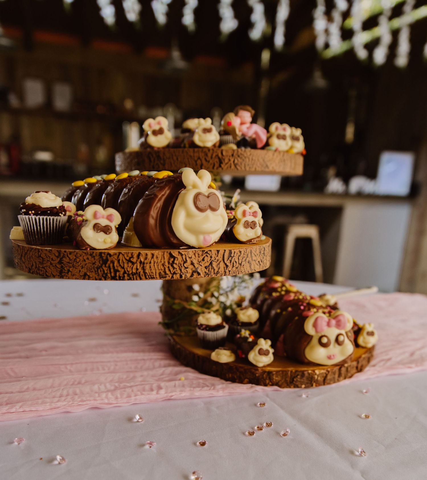 Chocolate cupcakes decorated with cute bunny faces made from frosting and candies arranged in a row on pink surface.