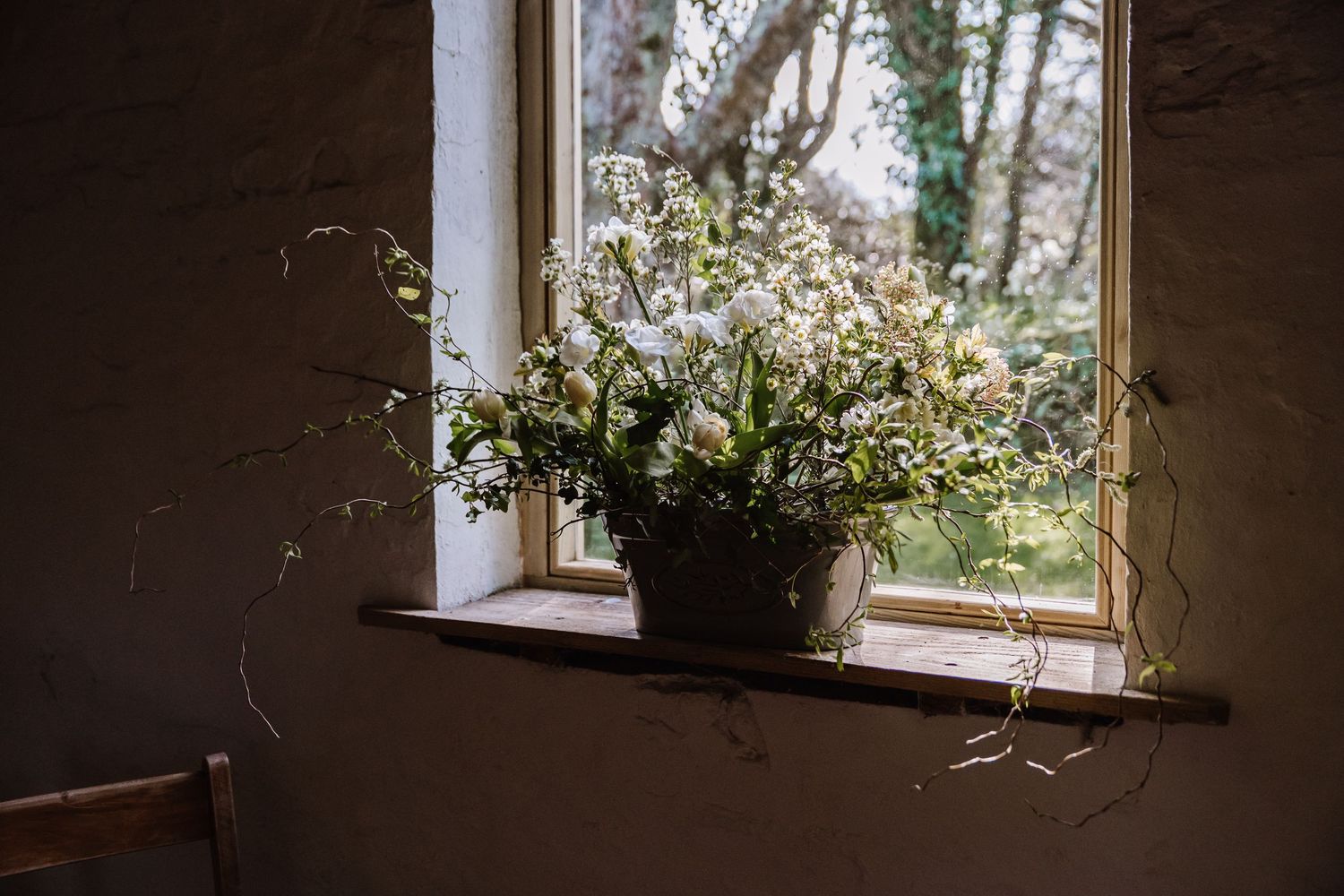 A rustic potted wildflower arrangement sits on a wooden windowsill, framed garden view. The Cornish Place, Wood shed wedding. Cornwall