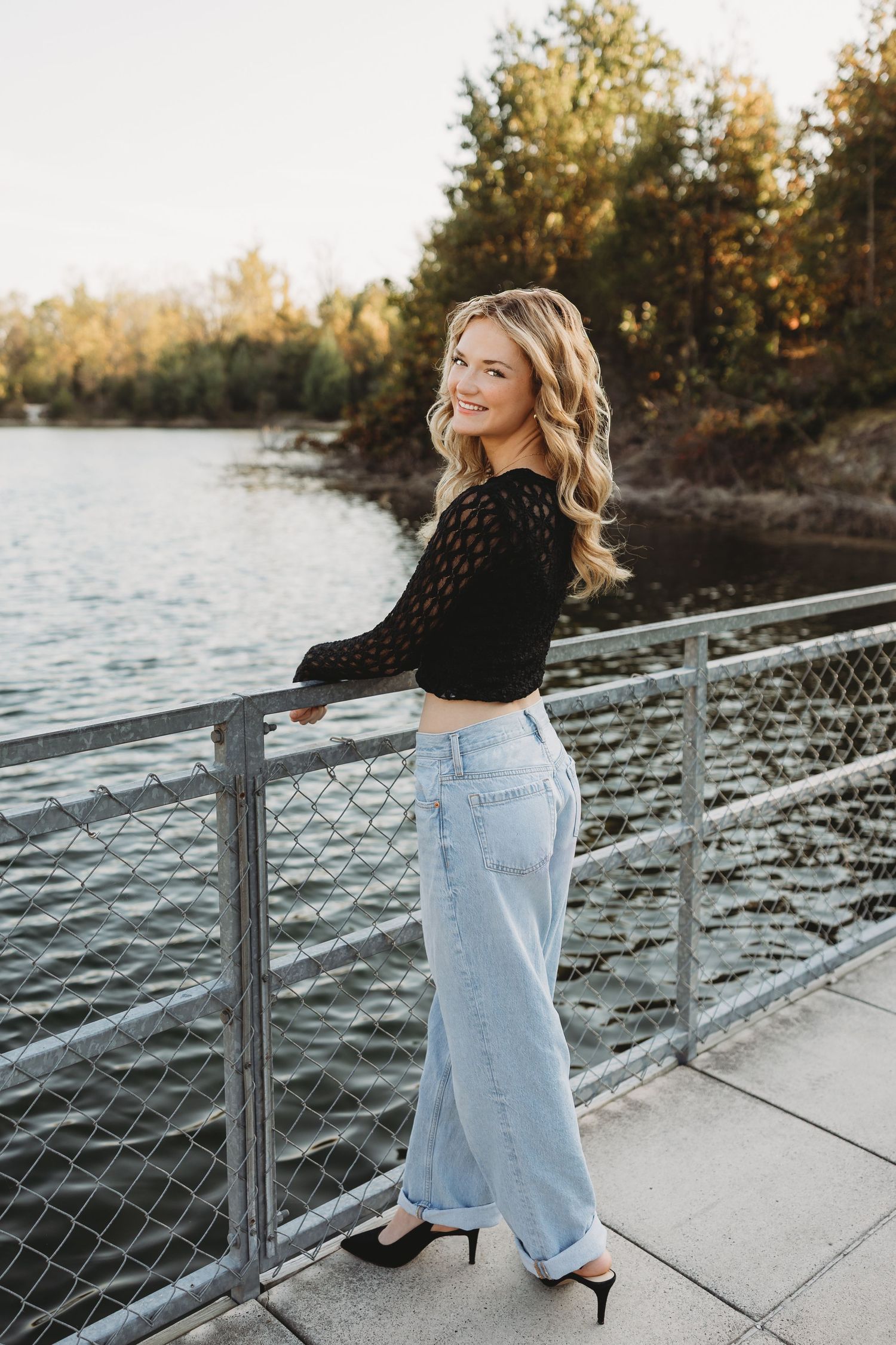senior girl Klondike park sunset golden hour water in background blonde hair blue jeans black top black heels