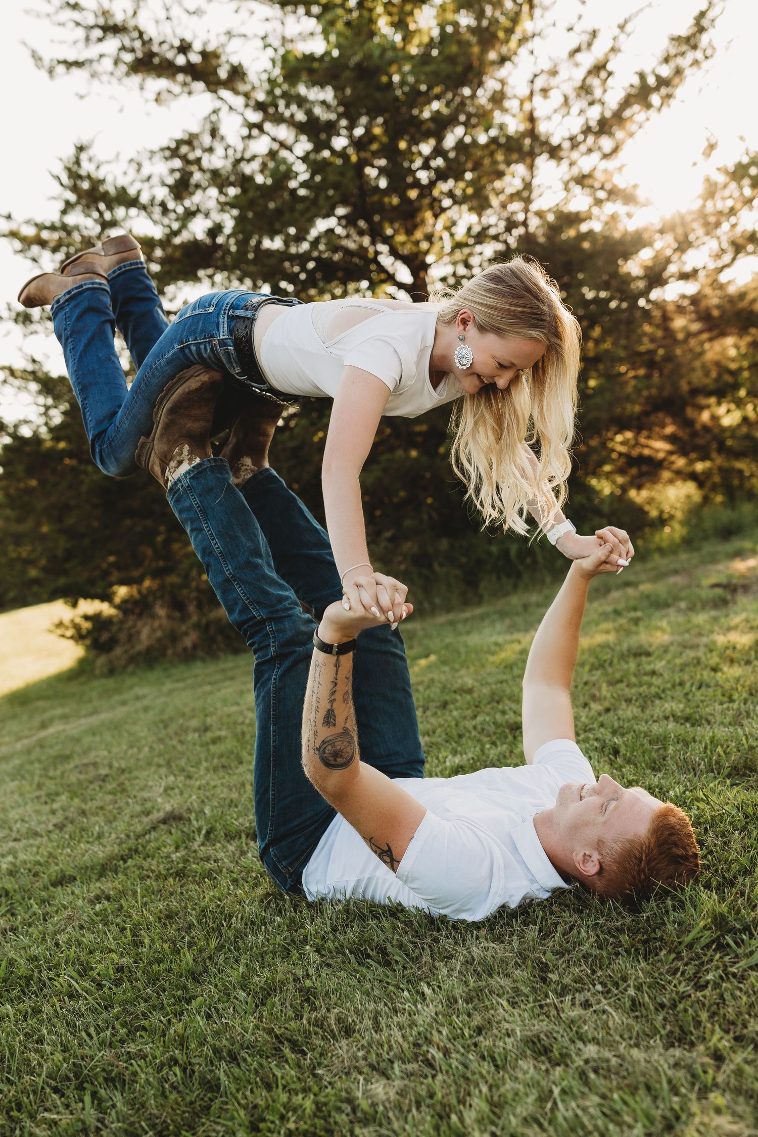 couple doing airplane in field white shirts blue jeans cowboy boots girl with long blonde hair guy with tattoos and is a marine