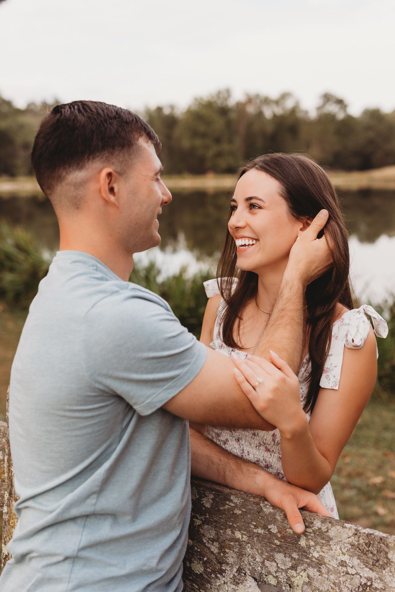 couple engaged golden hour light and airy embrace holding face laughing pond in background