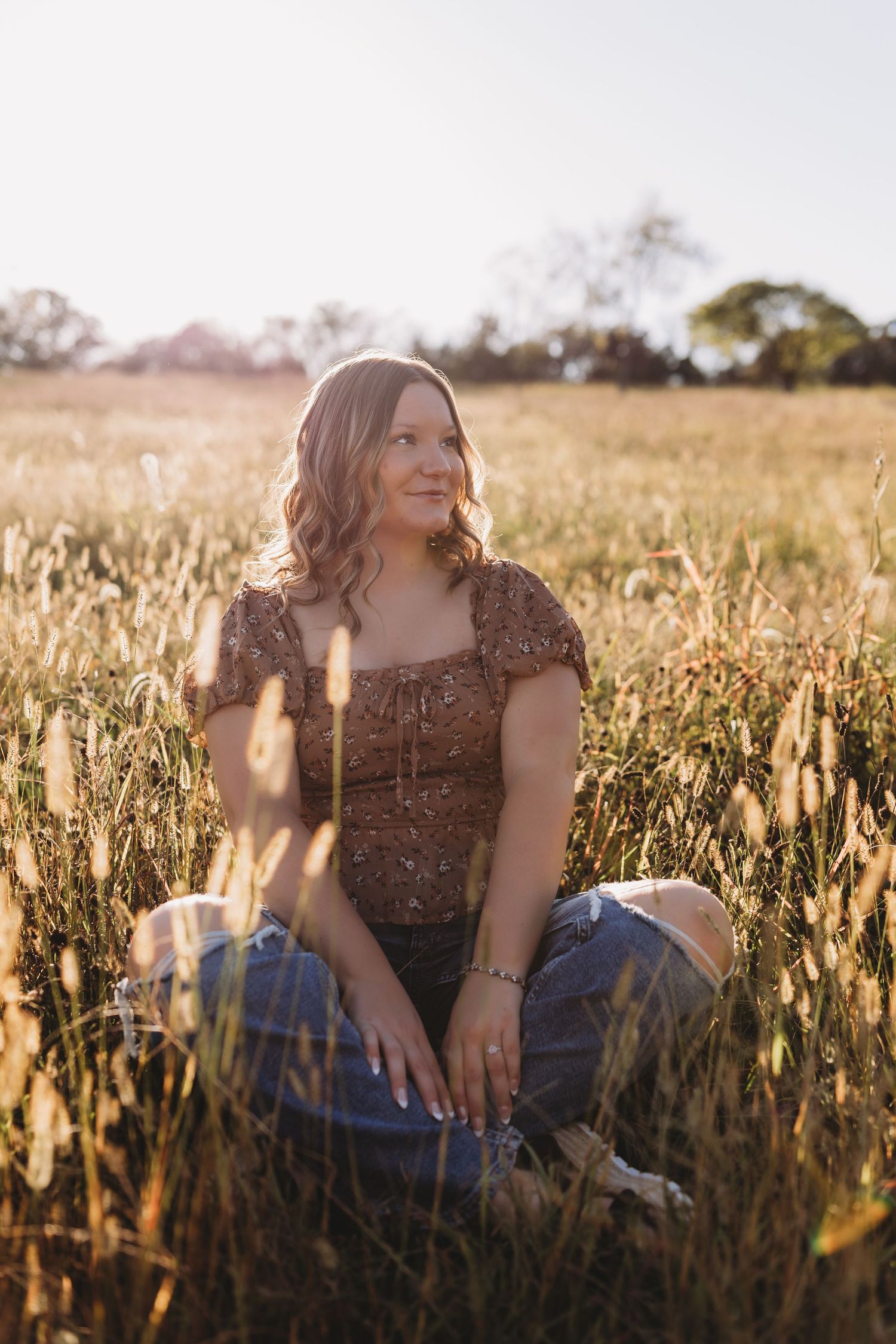 senior girl criss cross in field with golden sun behind her