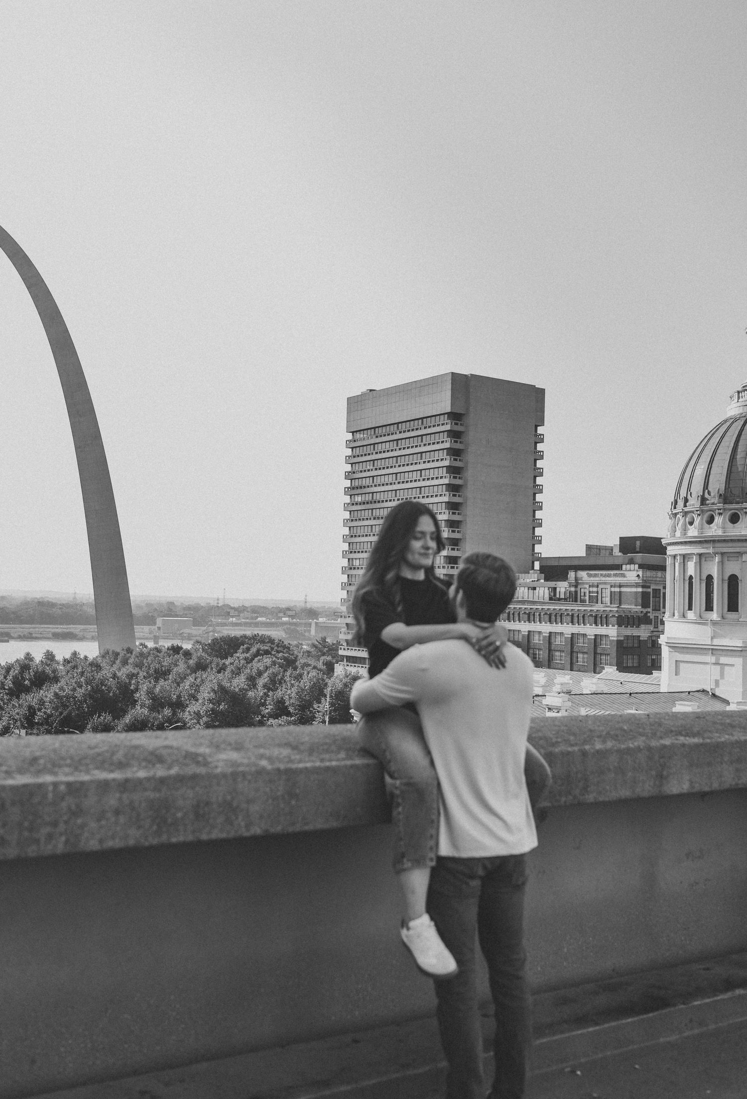 couple embracing on rooftop in st Louis with the arch behind them black and white photo