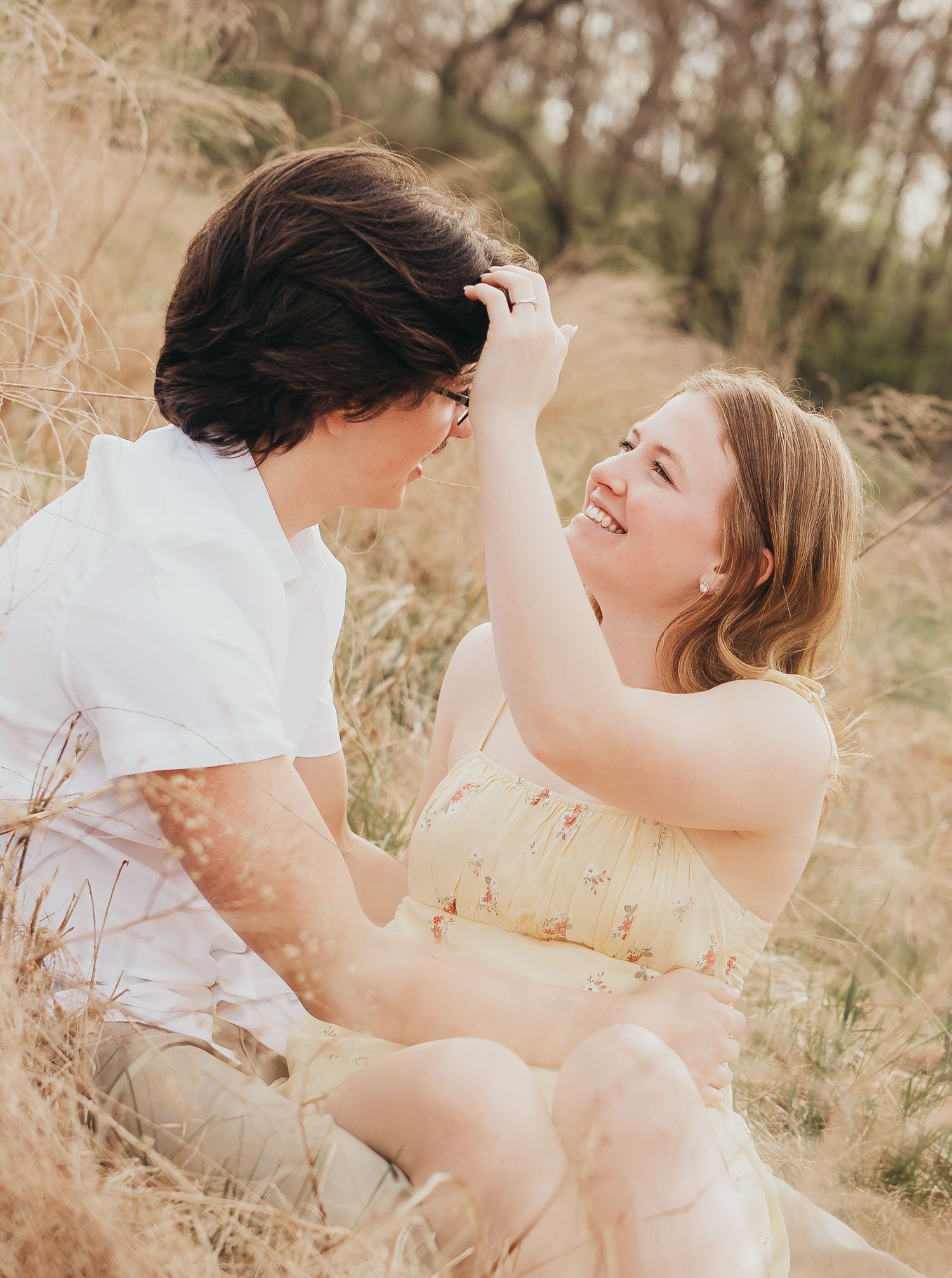 couple sitting in a field girl brushing guys hair back smiling whimsy