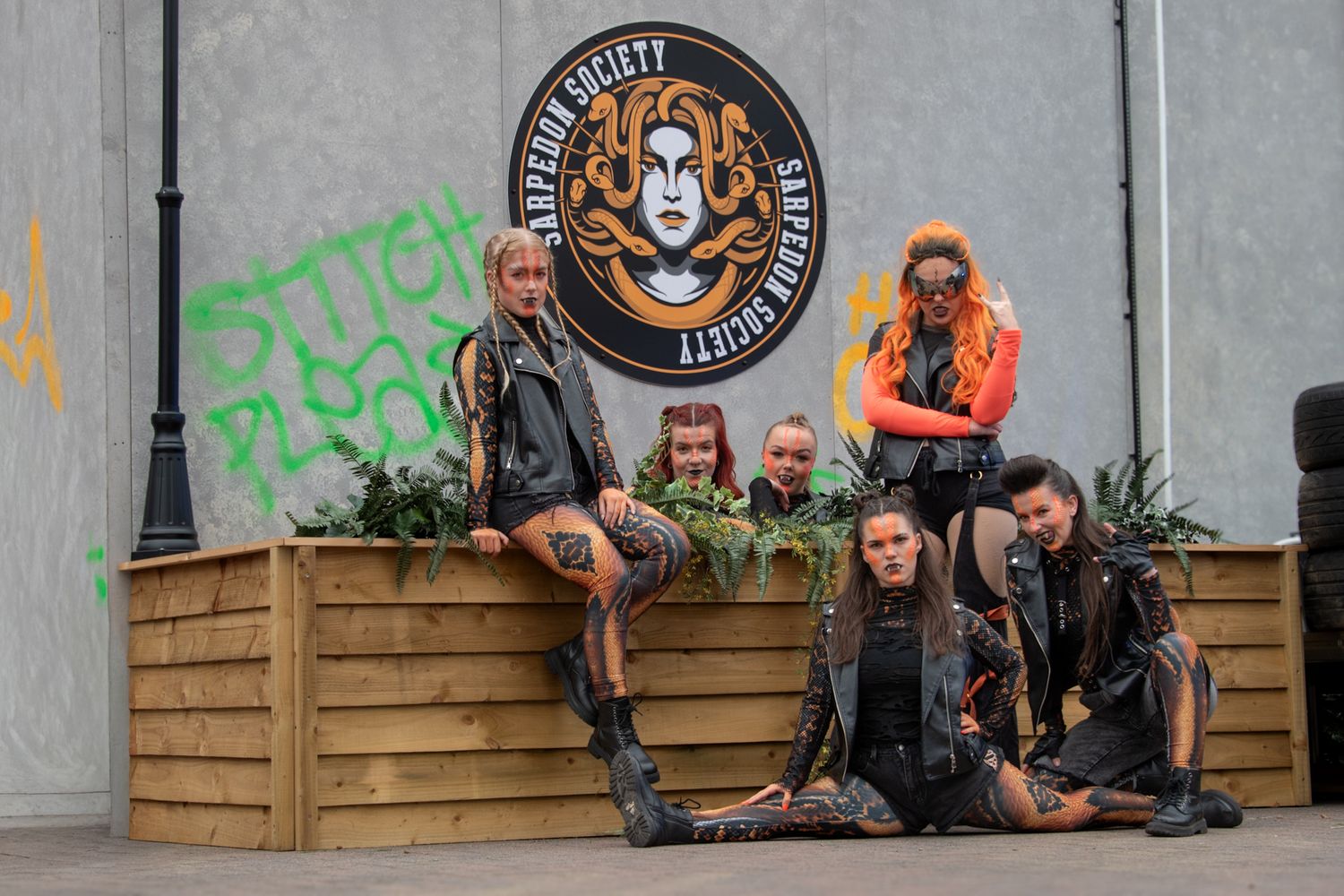 Group of six performers in post-apocalyptic costumes posing in front of a Gorgon Society themed backdrop.