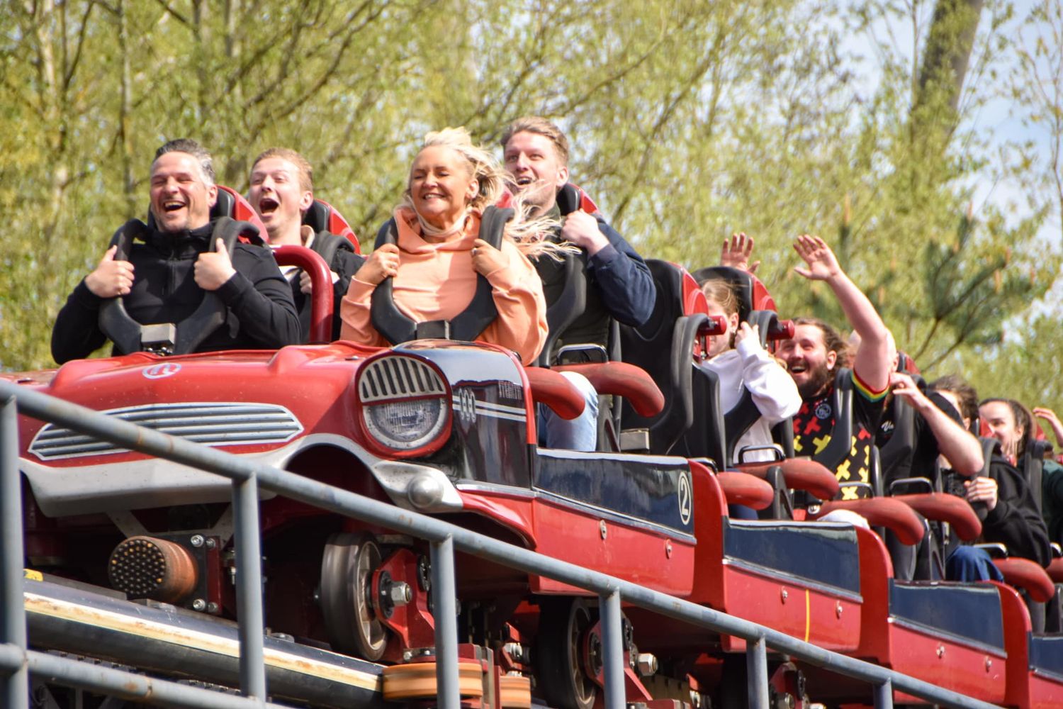 Excited group of people cheering on a red roller coaster ride at an amusement park.