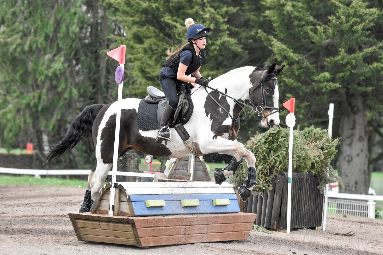 Rider on black and white horse jumping over cross-country obstacle at equestrian competition.