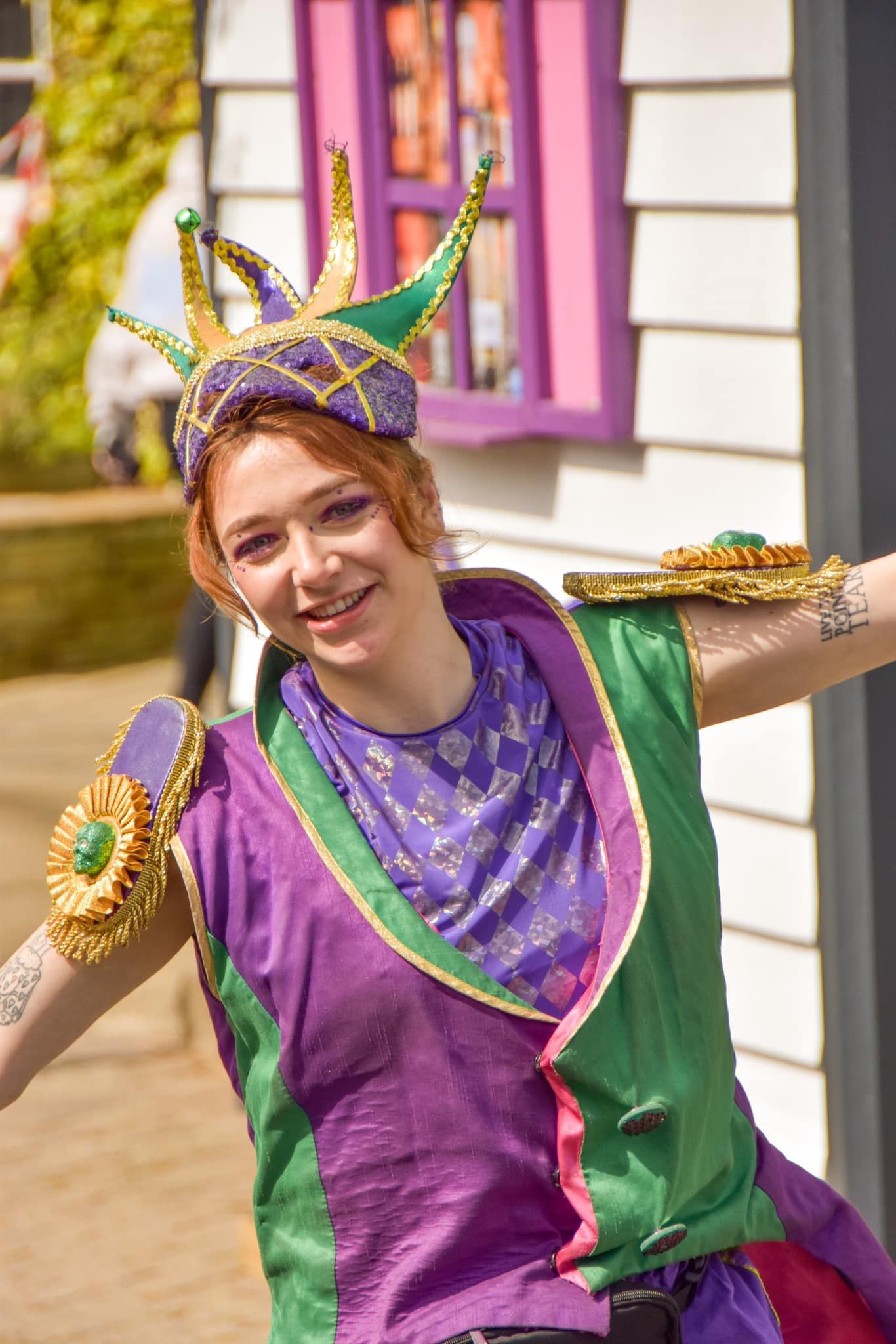 Cheerful female performer in colorful jester costume with crown dancing at an outdoor festival.