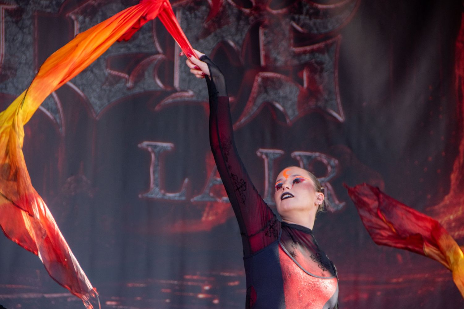 Female performer dancing with vibrant red and orange flowing fabric scarves under dramatic stage lighting.