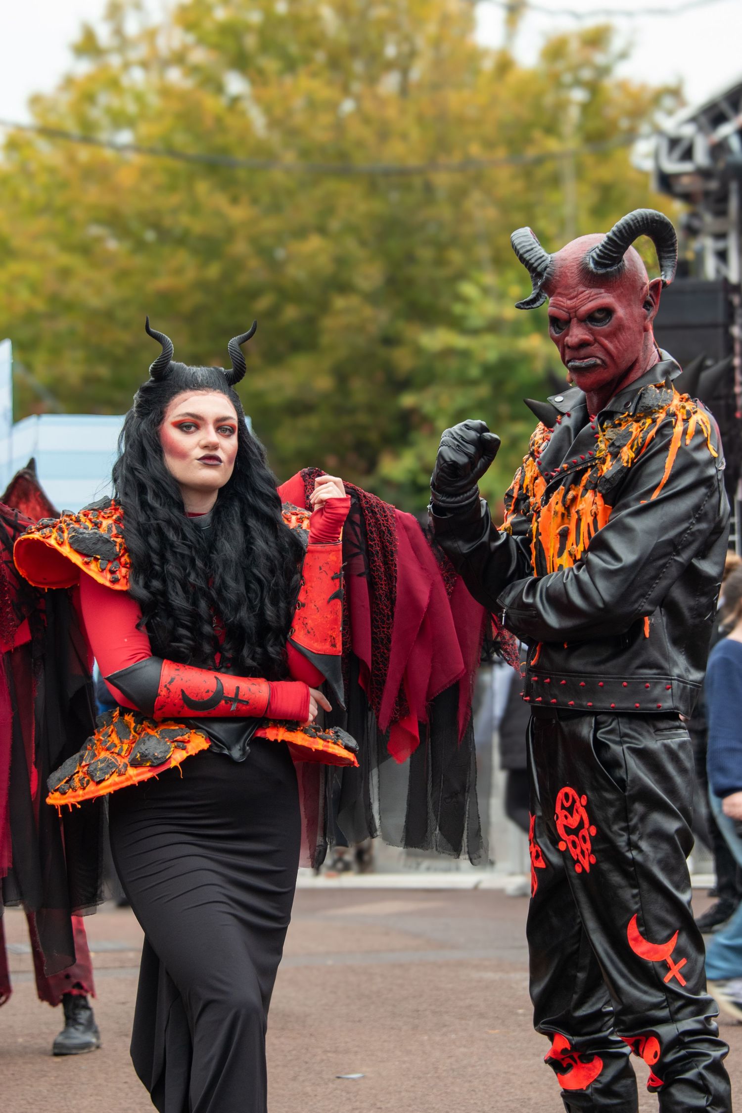 Couple in devil Halloween costumes with red body paint, black horns, and dramatic red and black outfits.