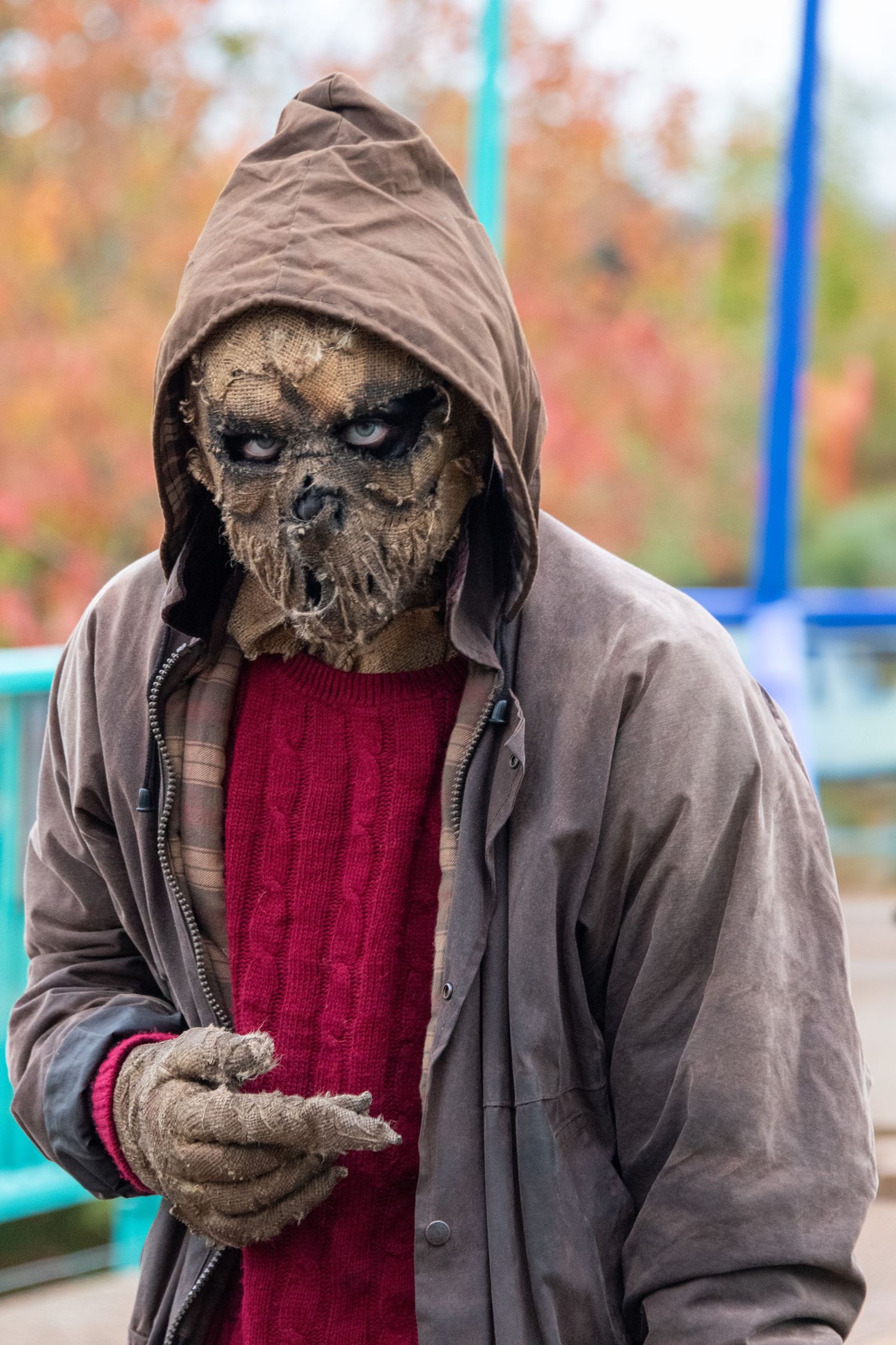 Person wearing scary scarecrow mask and hooded jacket in Halloween costume outdoors.
